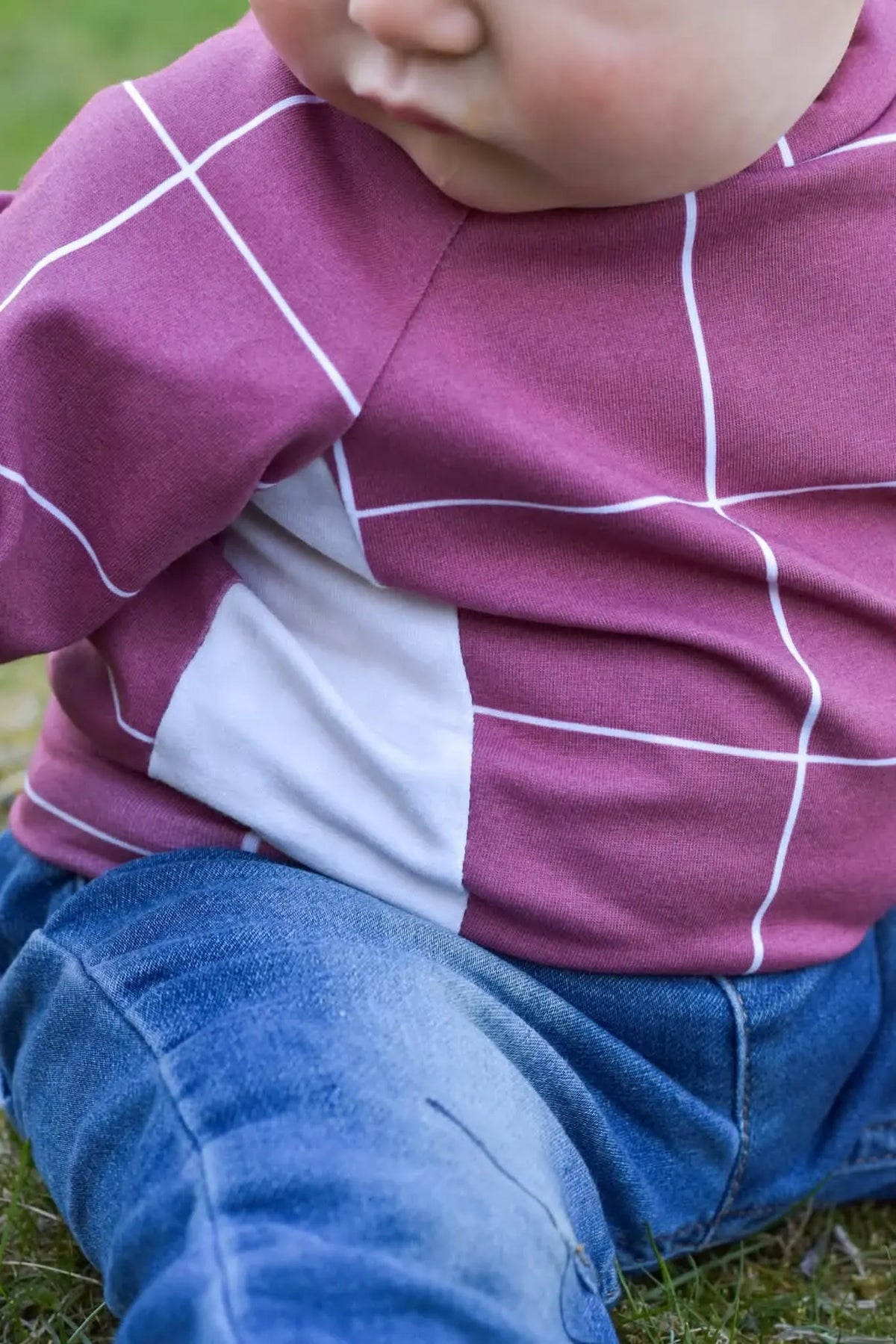 A child wears a red windowpane shirt with a white panel and blue jeans.
