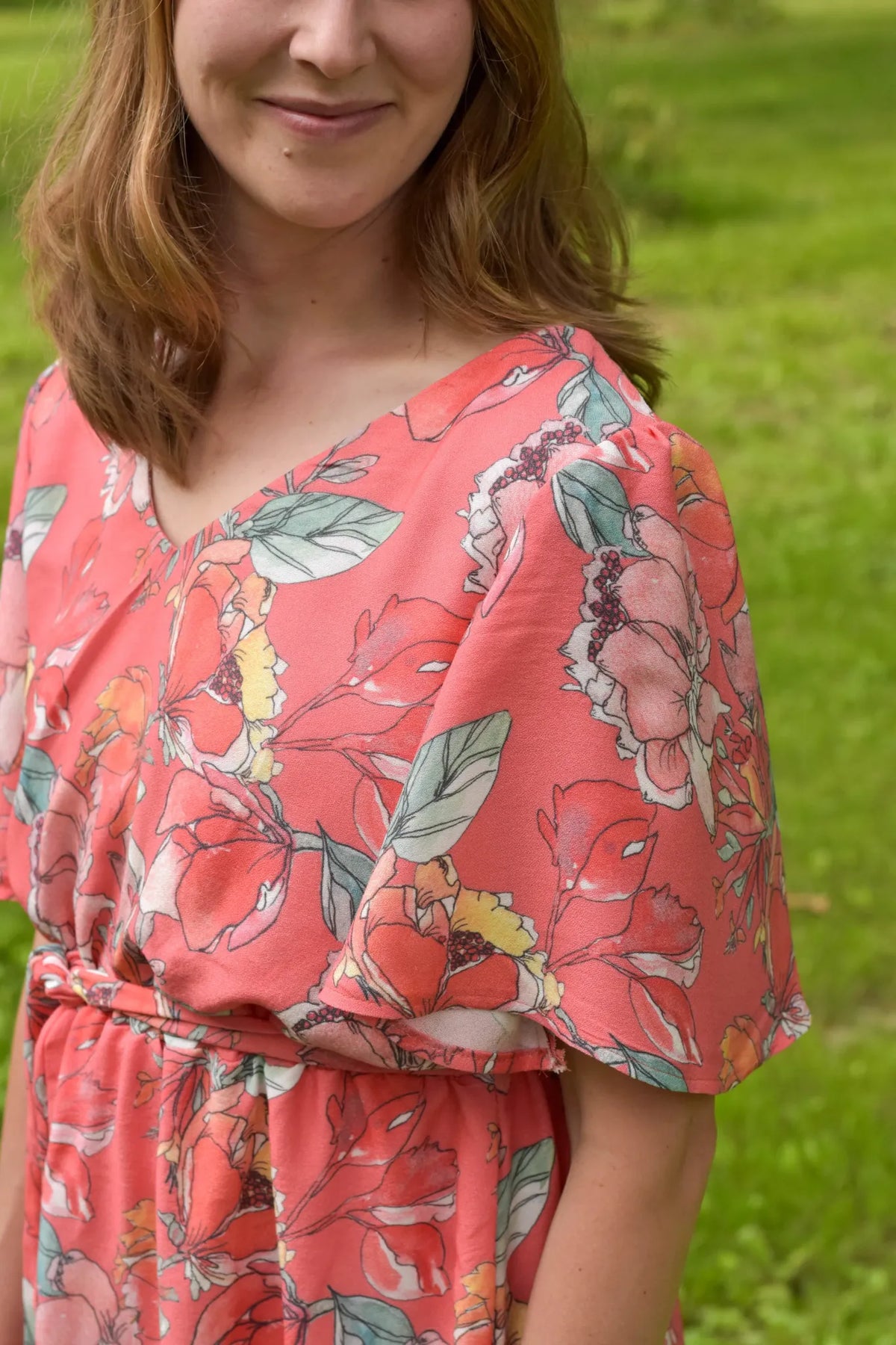 A woman in a coral floral dress with green leaves and yellow accents.