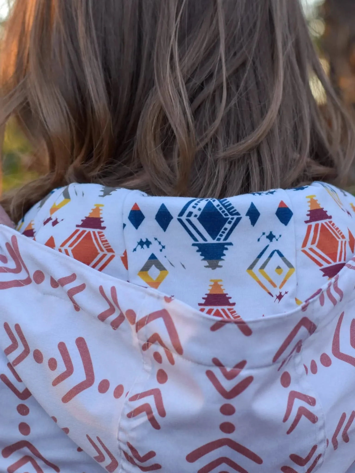 A person pulls back a white hooded garment with a desert diamond pattern.