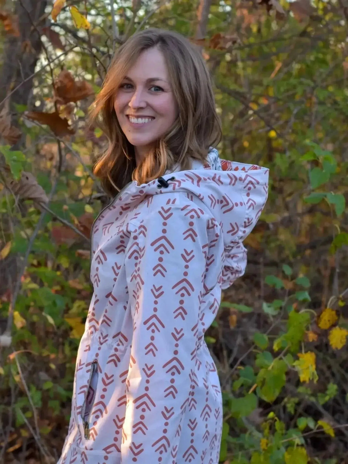 Woman modeling terracotta echoed steps abstract print rain jacket with hood in autumn woods.