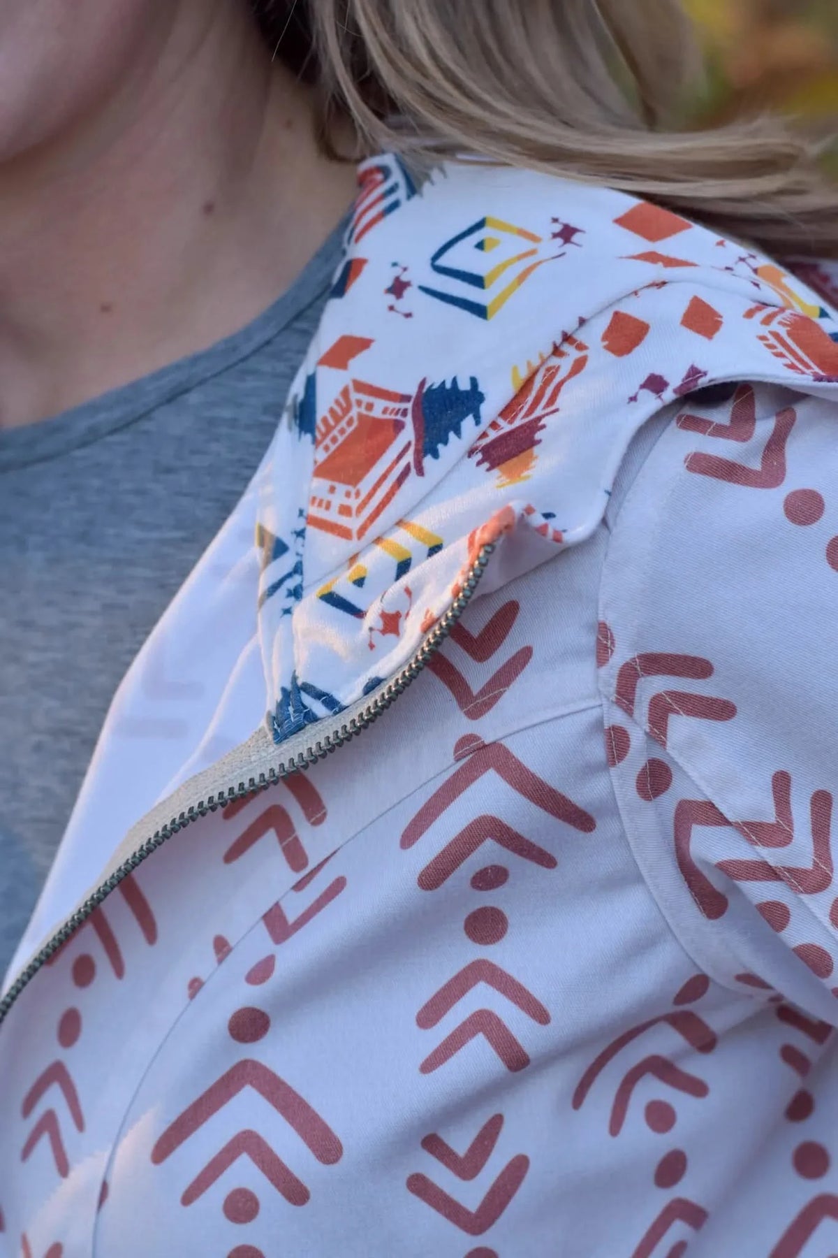 A person wears a white jacket with colorful geometric patterns and a grey shirt.