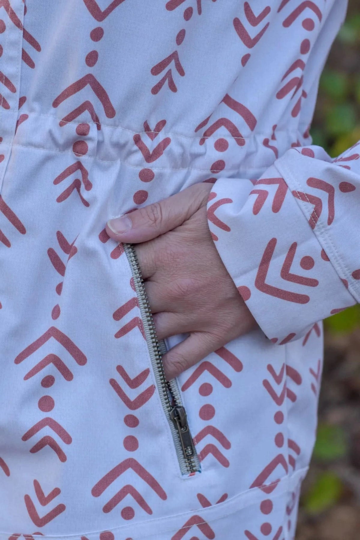 A person's hand is in the pocket of a white garment with a rust-colored pattern.
