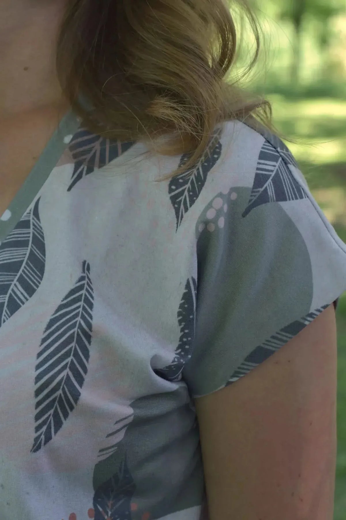 A person wears a shirt with a gray and pink leaf pattern.