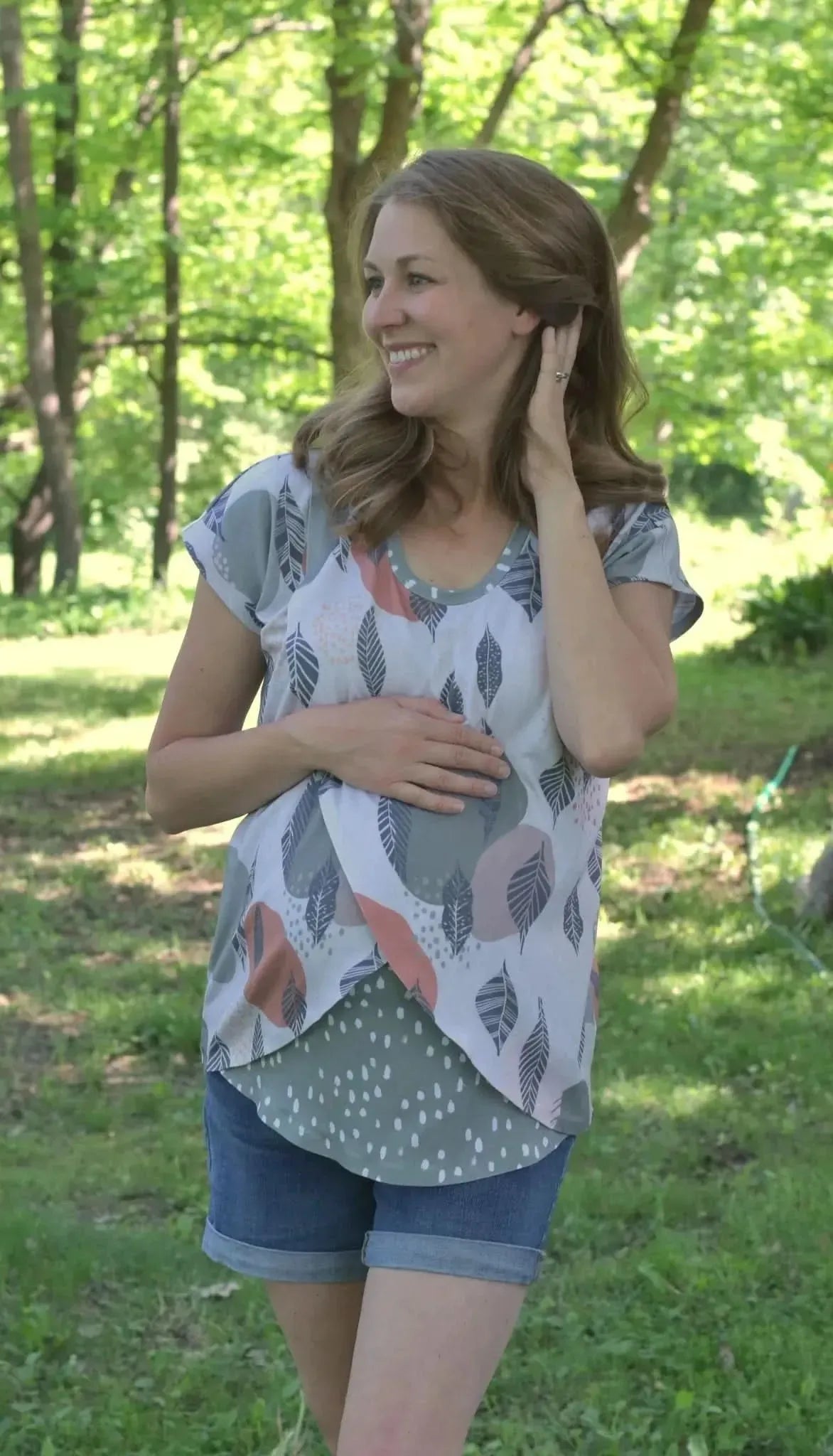 A woman in a Mod Leaves top and denim shorts smiles in a park.