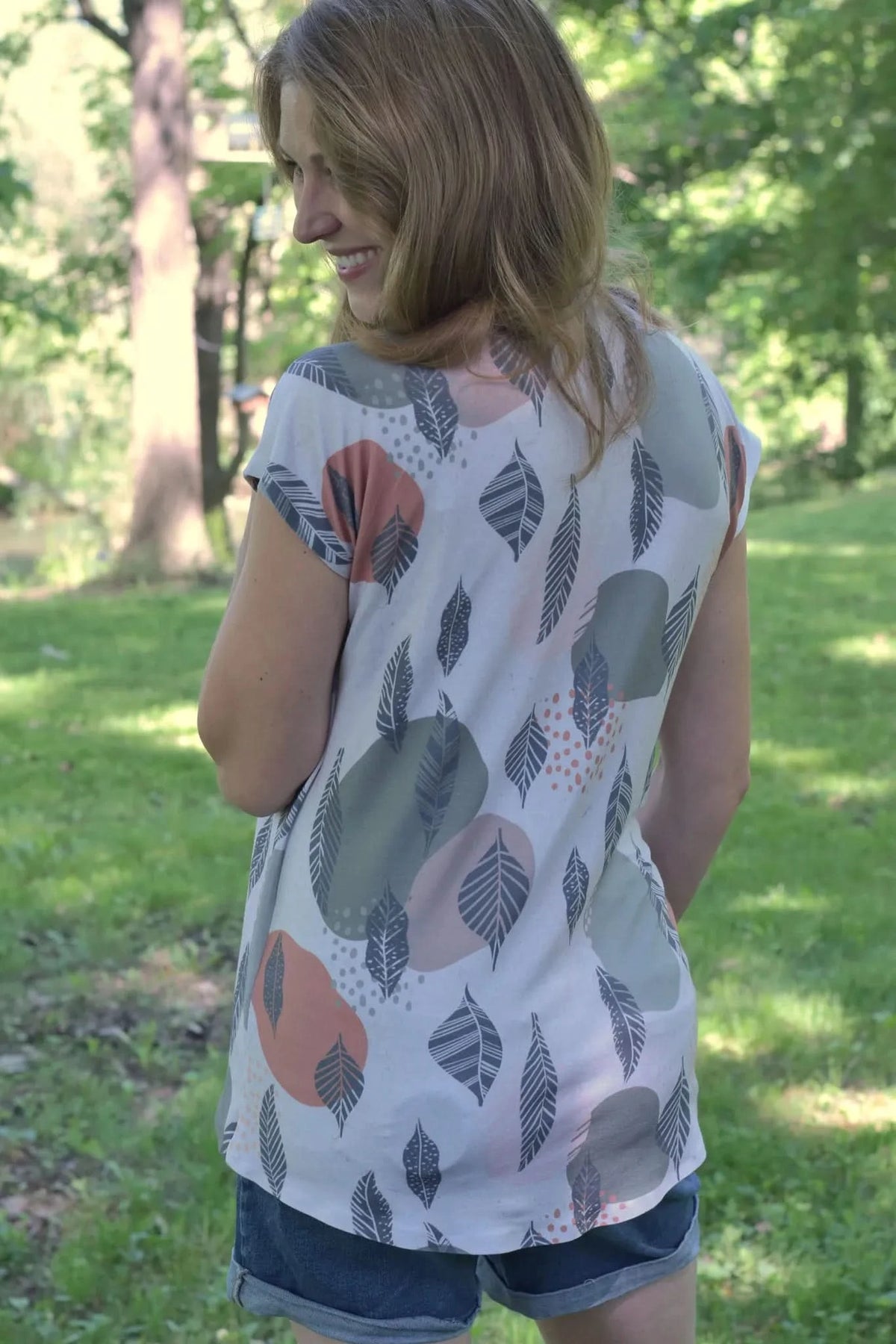 A woman from behind wears a Mod Leaves patterned top and denim shorts outdoors.