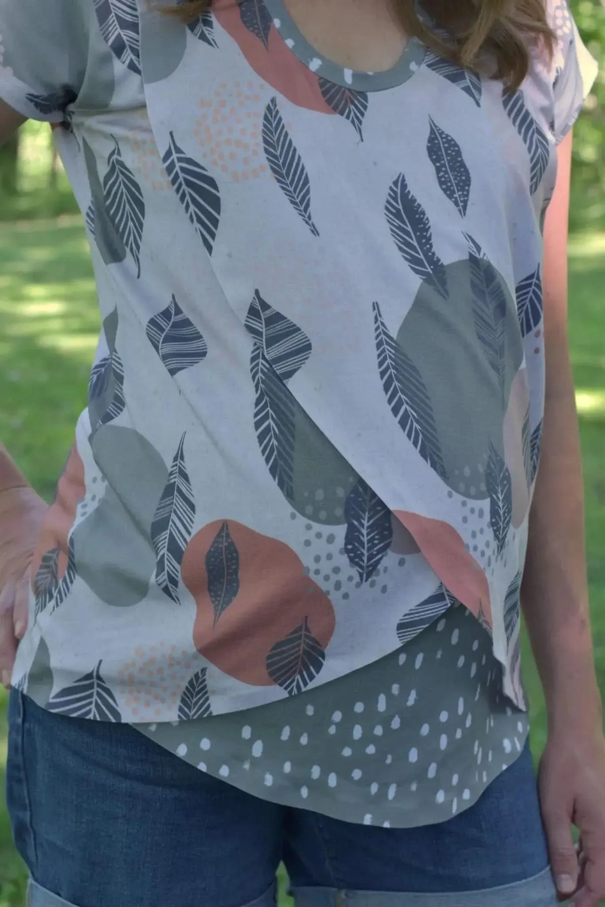 A person wears a shirt with a mod leaves pattern and blue jeans.