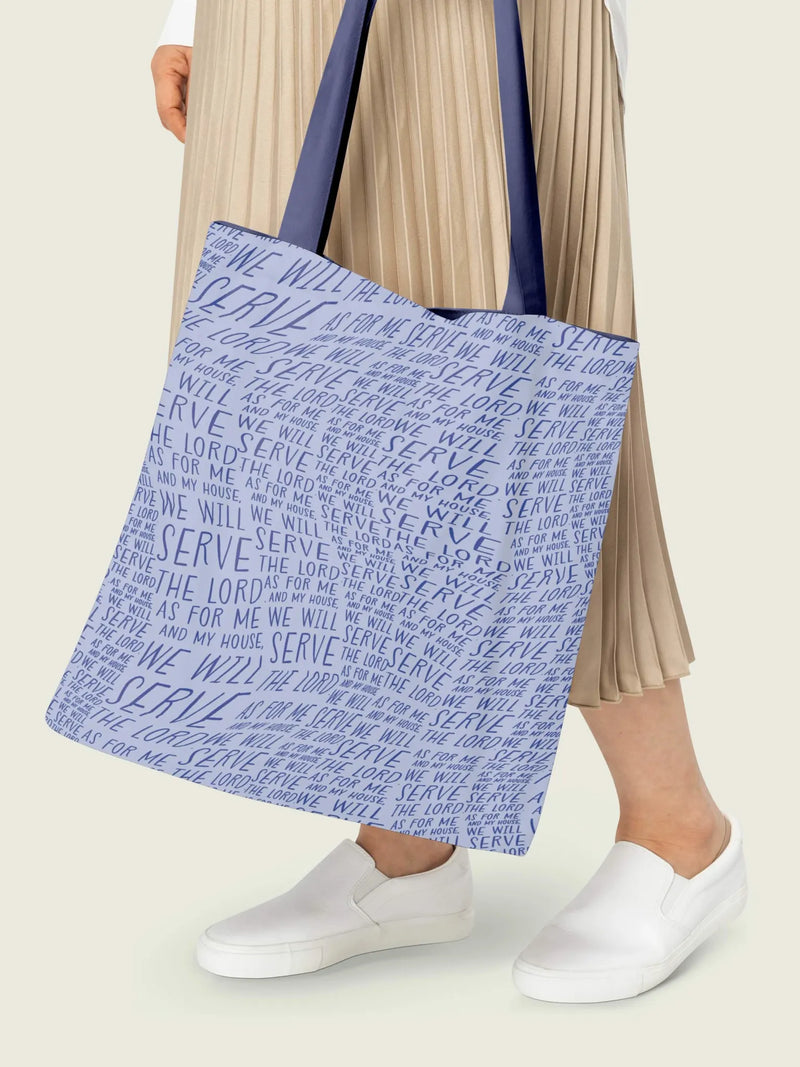 Light blue tote bag with "Serve the Lord" text, held by a person in a pleated skirt.