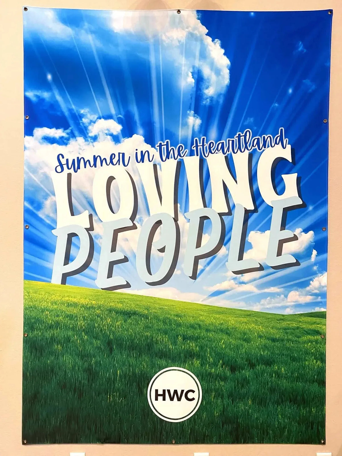 A banner with a blue sky, green grass, and the words "Summer in the Heartland Loving People."