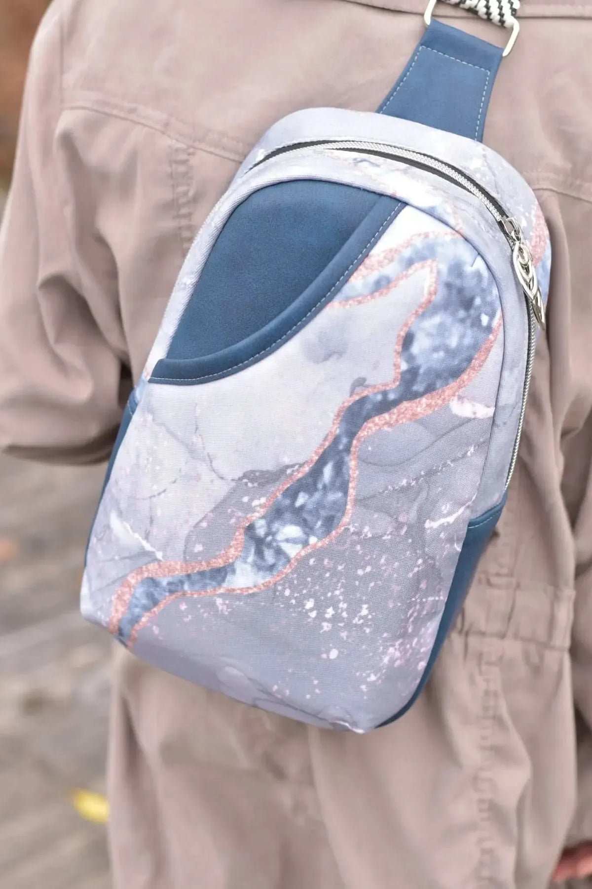 A blue marble sling bag with rose gold accents is worn over a tan jacket.