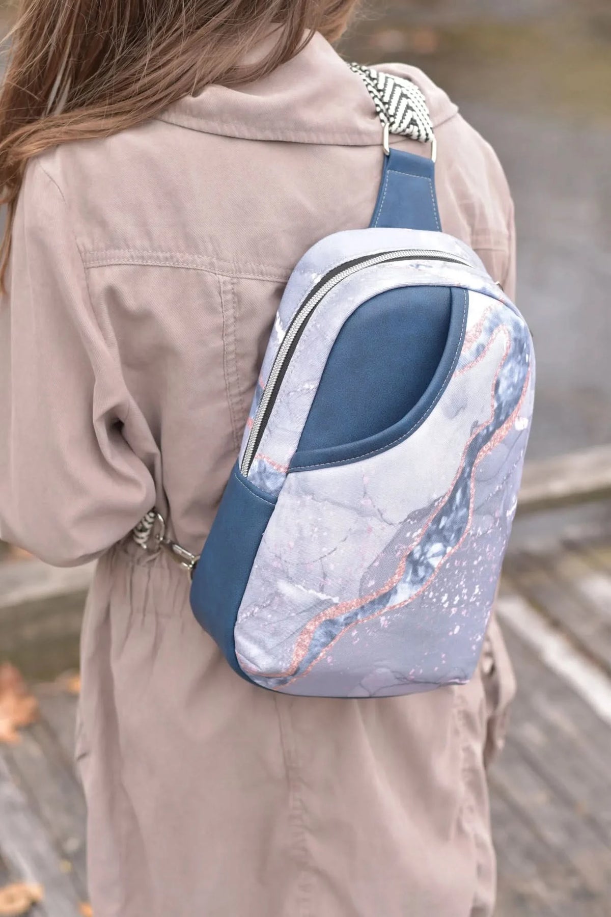 A person wearing a beige jacket and a blue marble sling bag.
