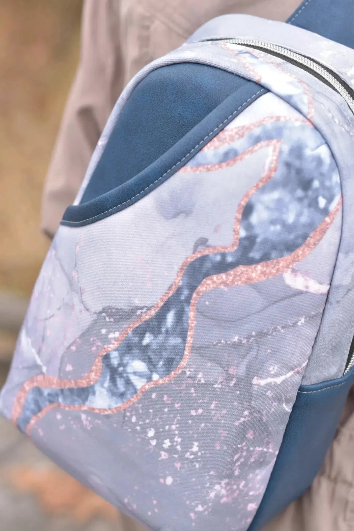 A close-up of a bag made from blue marble pattern fabric with rose gold accents.