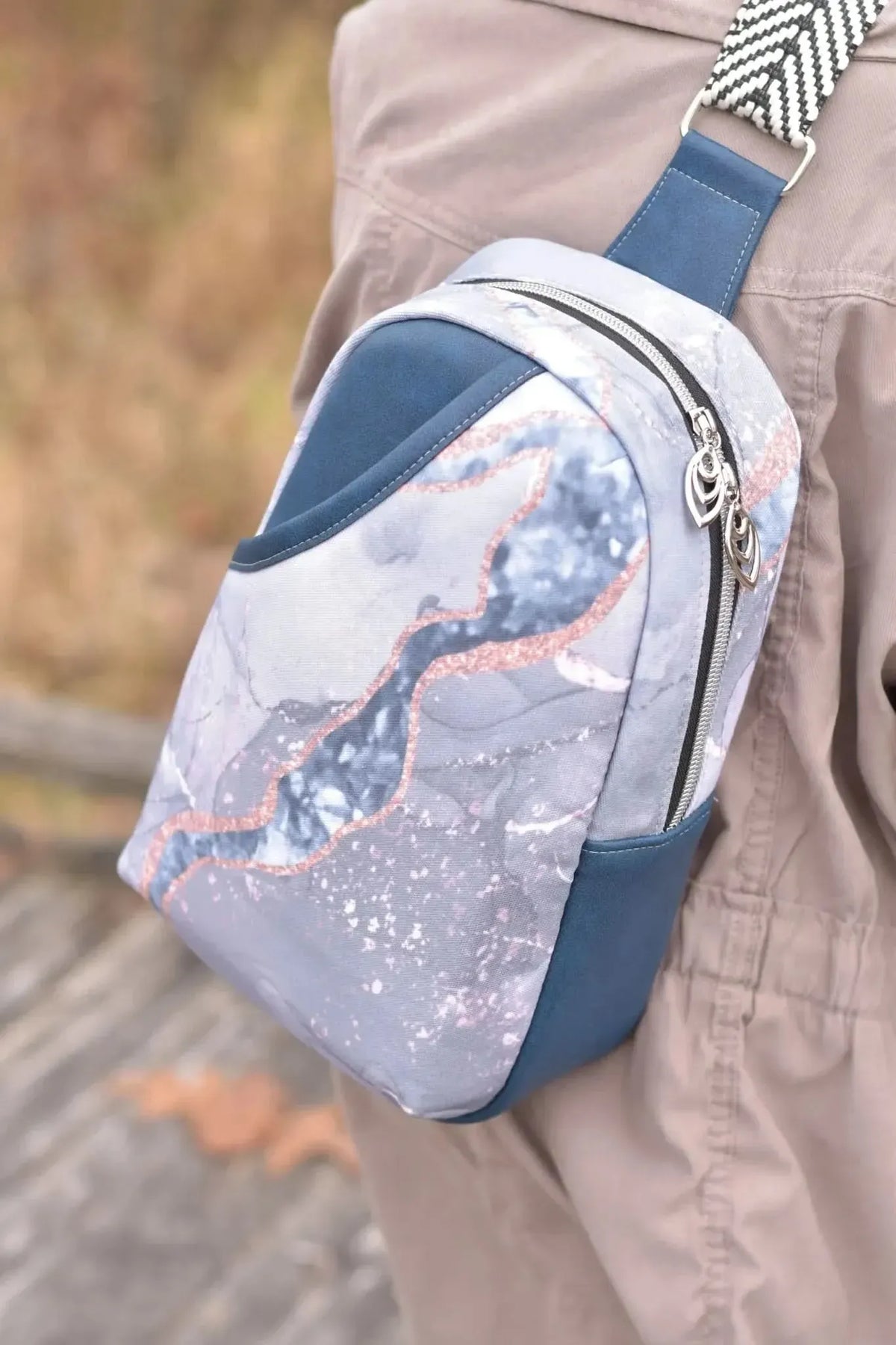 A person wears a blue marble print sling bag with a black and white strap.