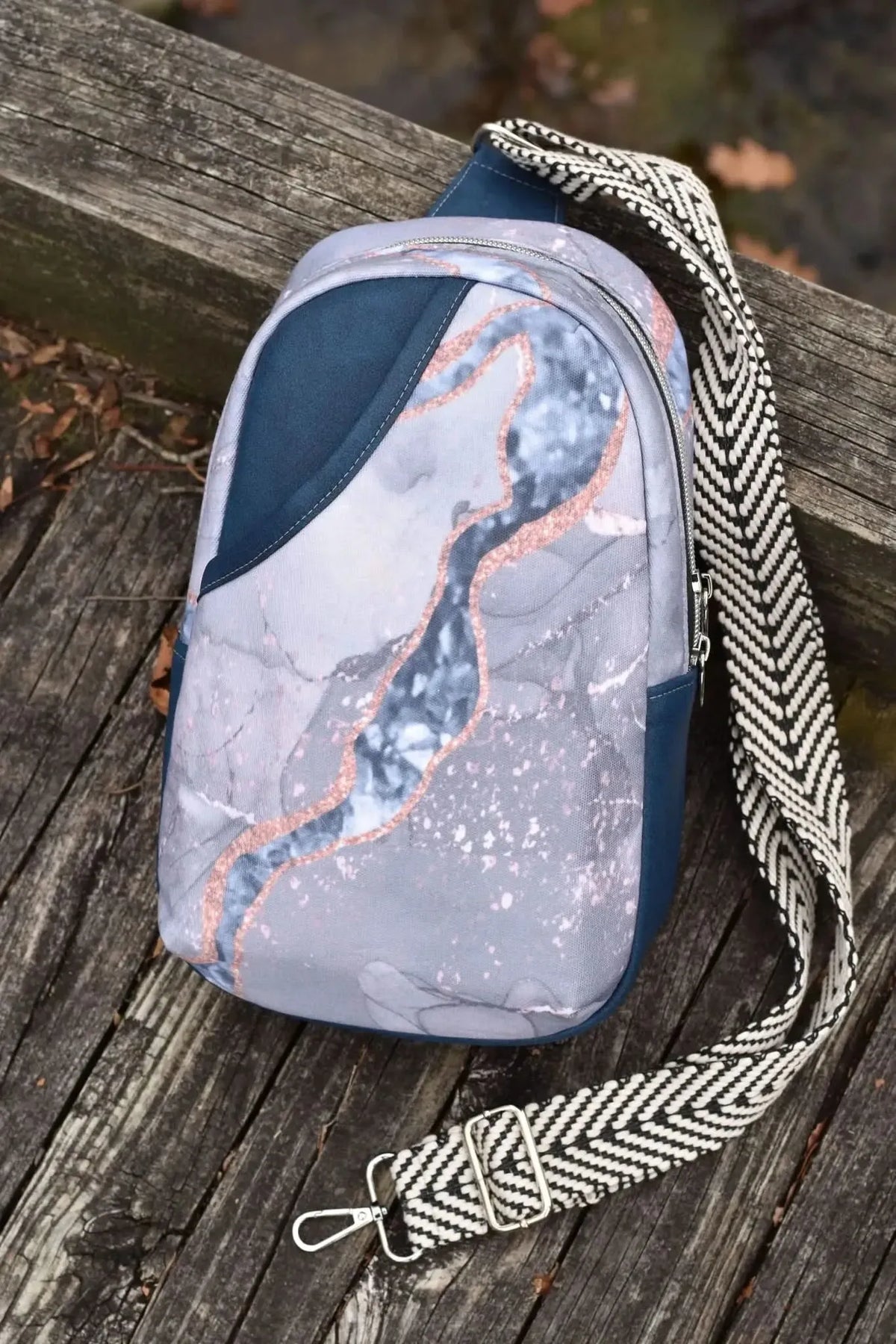 Blue marble sling bag with a black and white chevron strap on a wooden surface.
