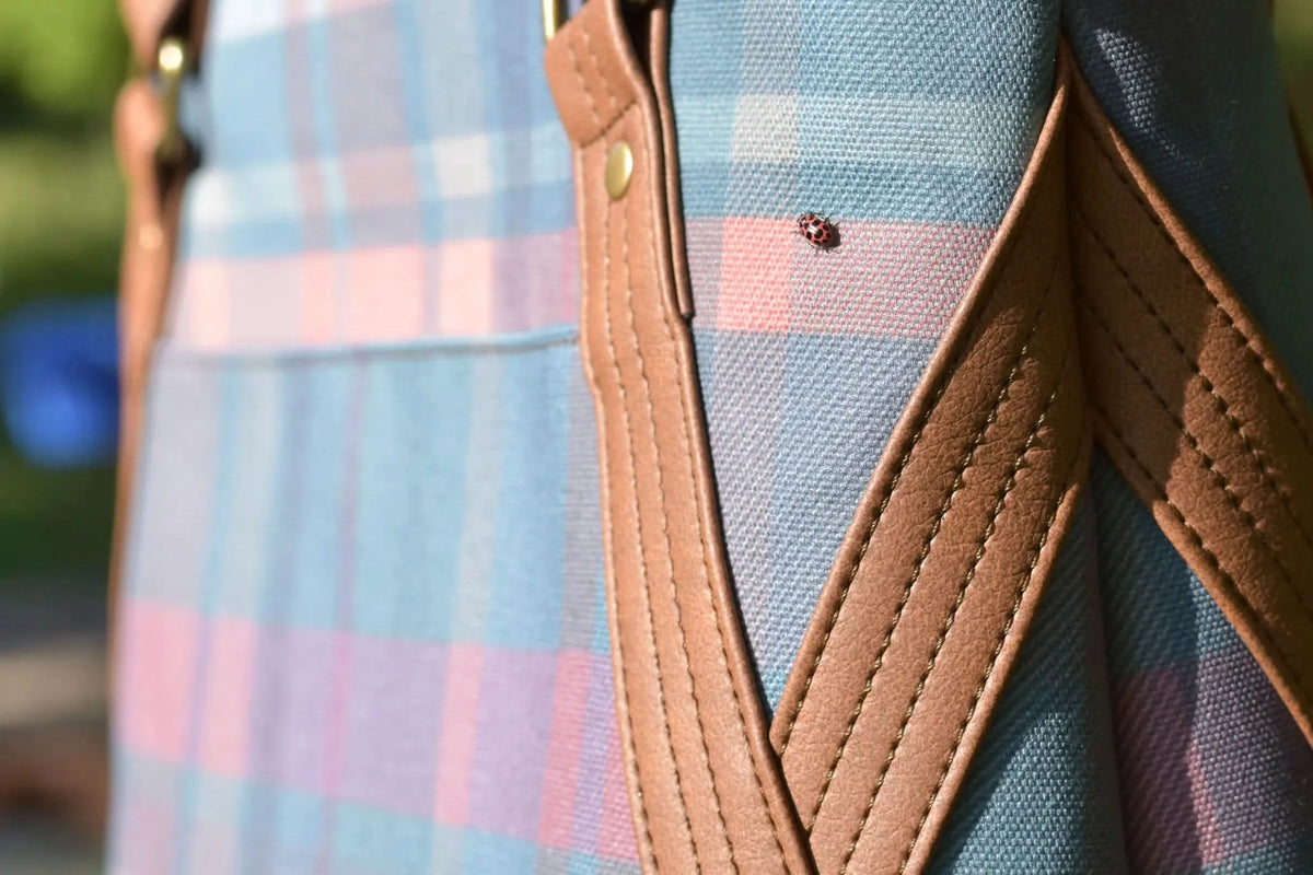 A ladybug rests on a blue, pink, and purple plaid fabric with brown leather straps.