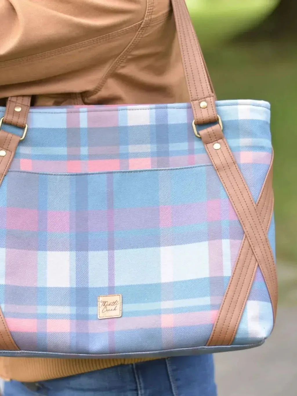 A person carries a plaid tote bag with brown leather straps.