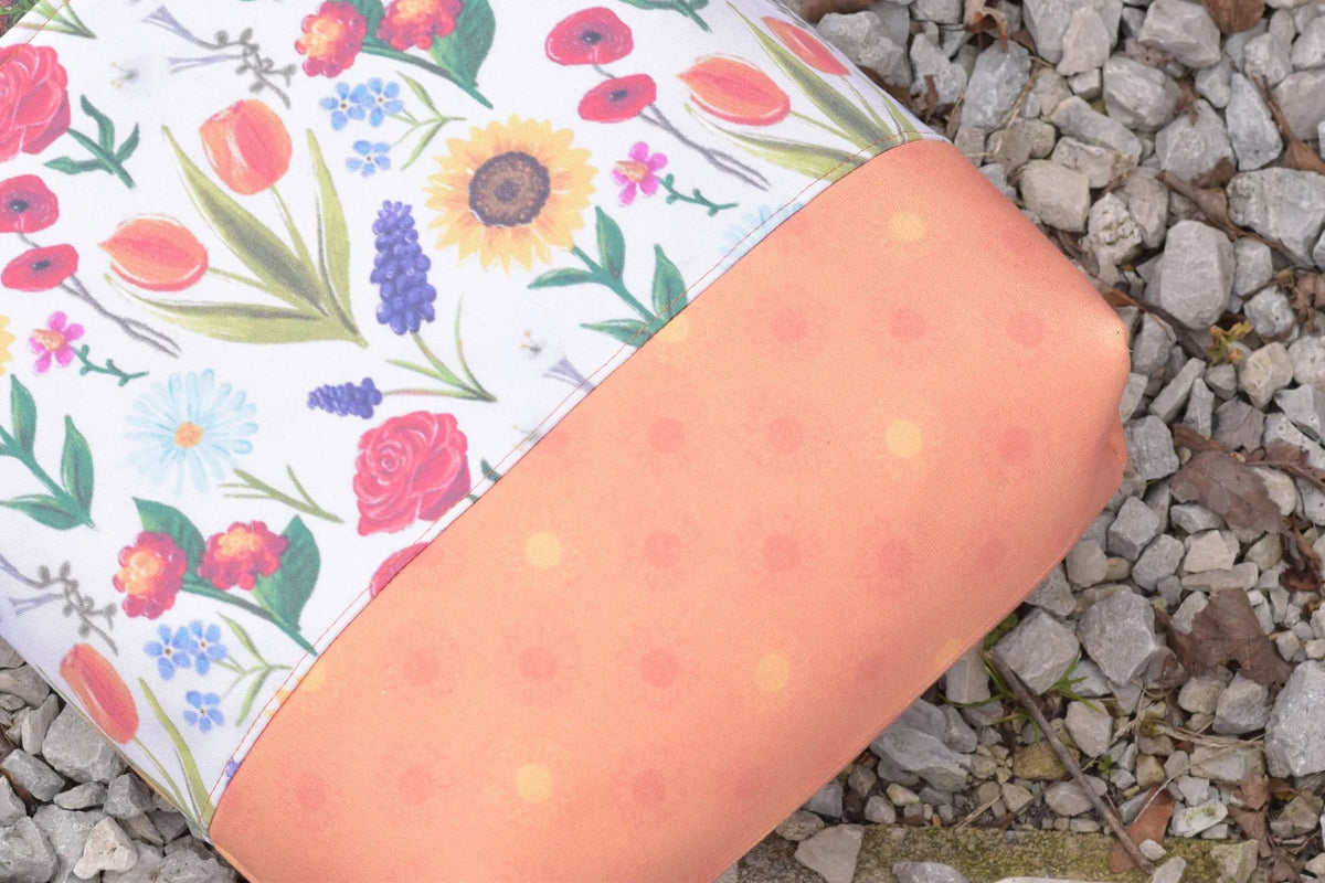 A fabric with a floral pattern and a solid orange section rests on a bed of gravel.