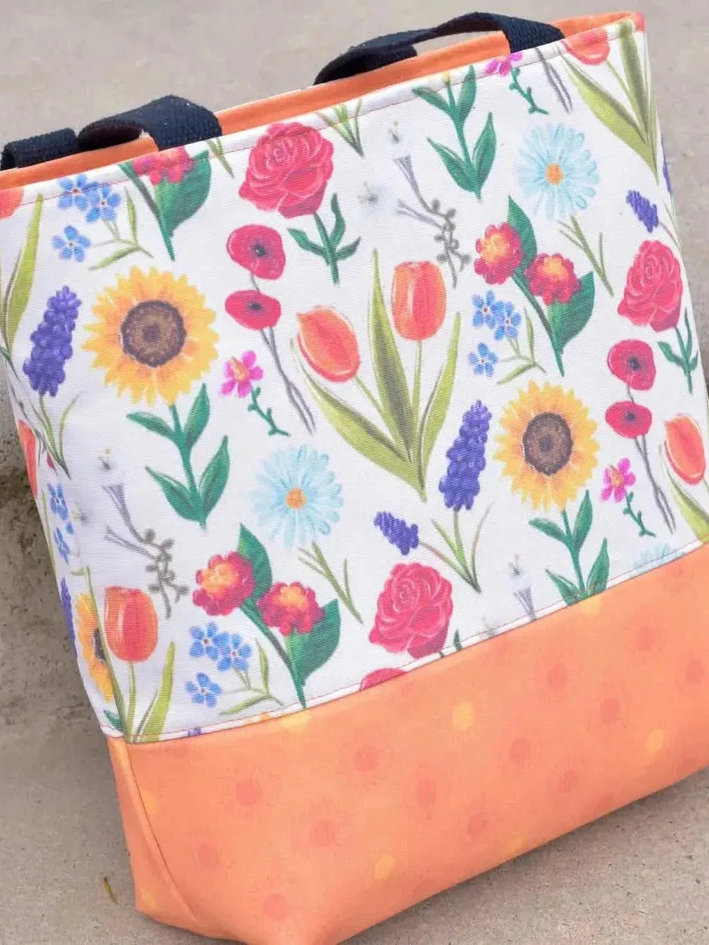 A tote bag with a vibrant floral print and an orange polka dot bottom.