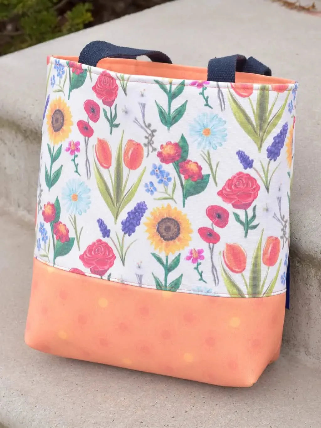 A floral tote bag with a white background and an orange bottom panel.