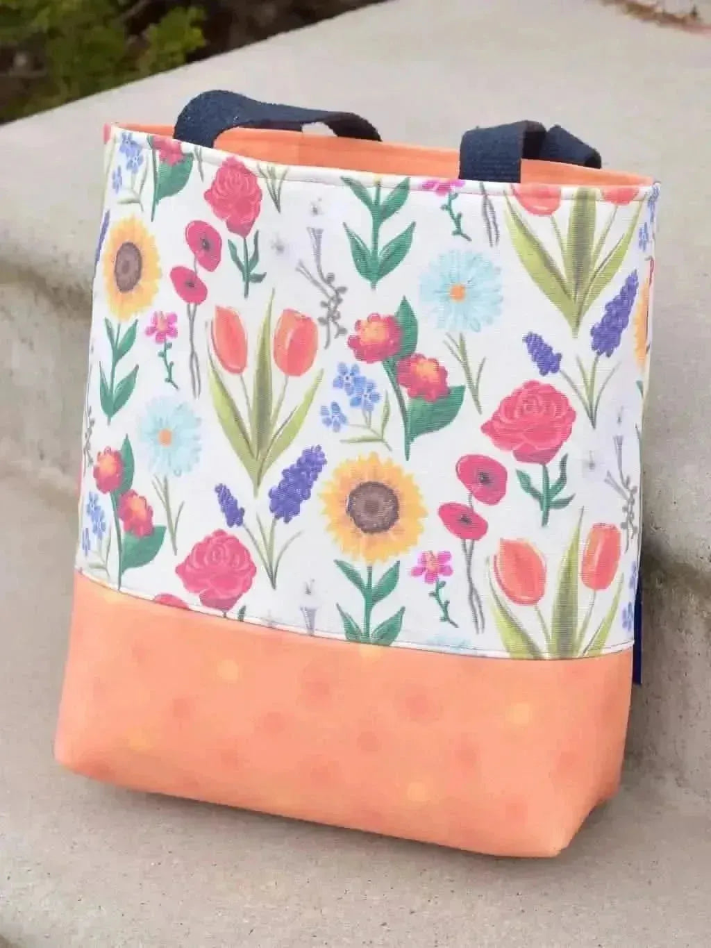 A tote bag with a vibrant floral print and an orange bottom.