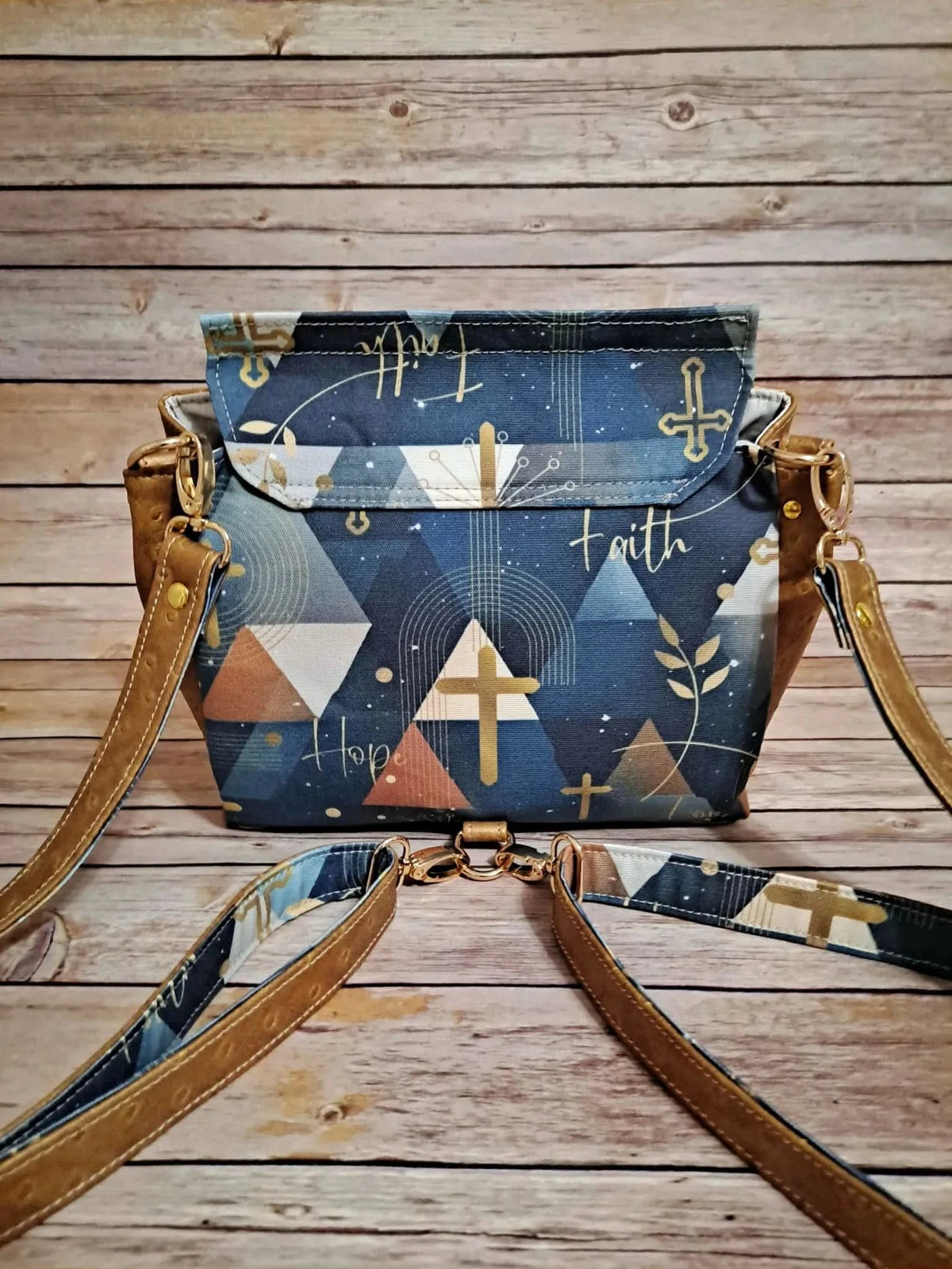 A blue and brown bag with a cross and "faith" pattern, on a wooden surface.