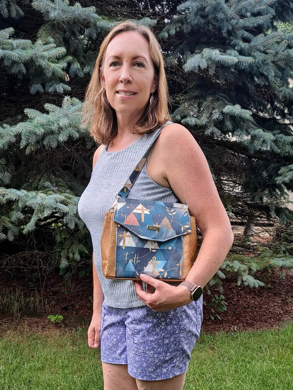 A woman holds a blue and brown handbag with "Hope" and "Faith" written on it.