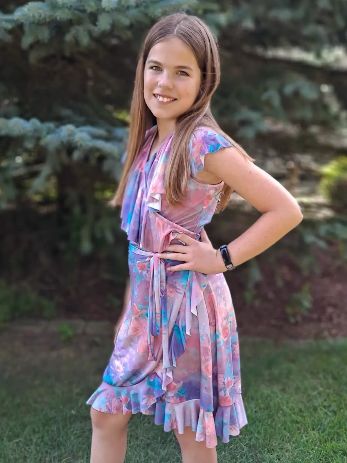 A young girl in a purple floral dress with ruffles and a tie waist.