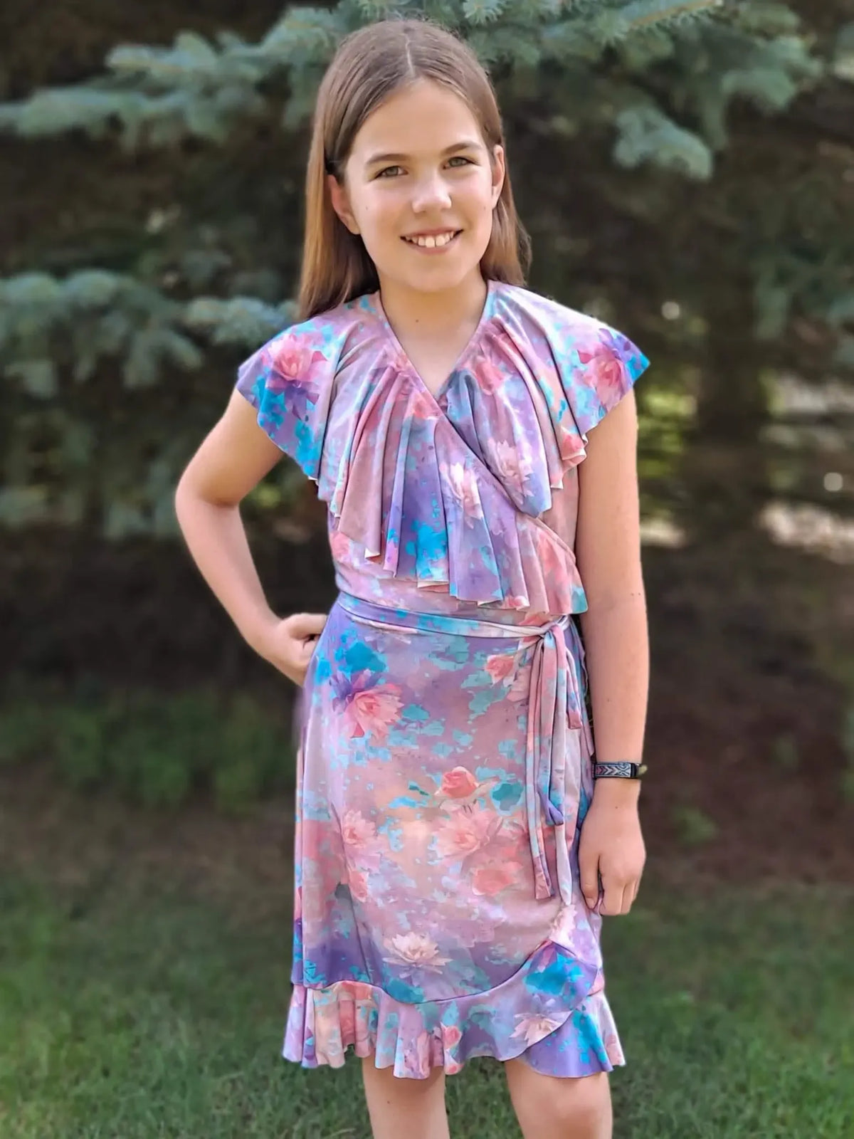 A young girl wears a purple floral dress with ruffles and a tie waist.