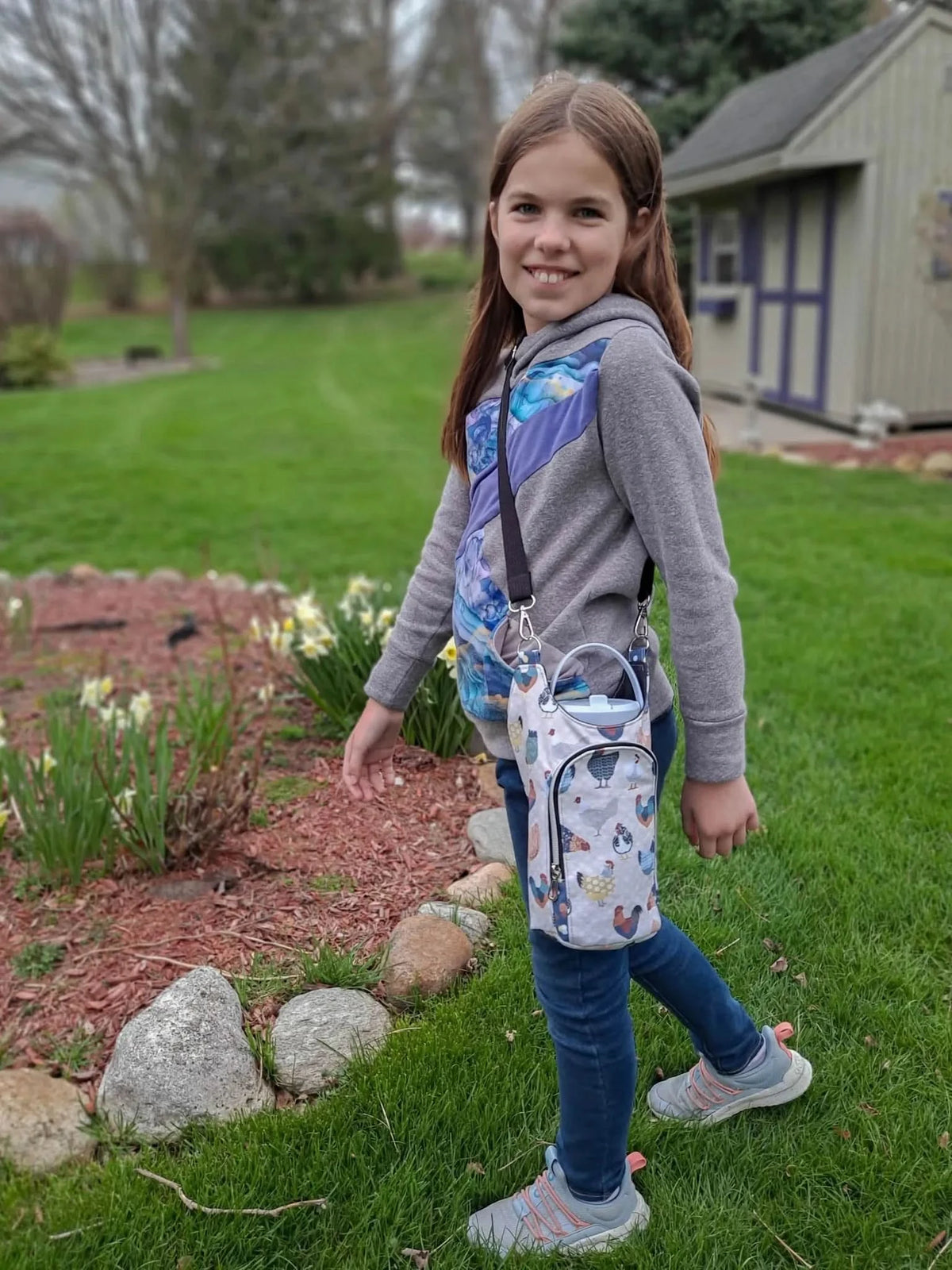 A girl wears a gray hoodie with blue and purple fabric inserts and a chicken-patterned bag.