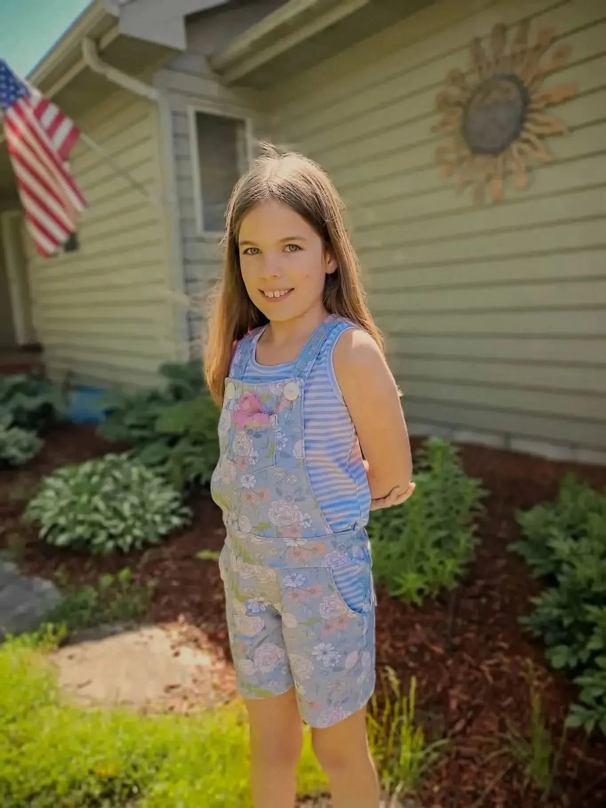 Girl wearing overall shorts made from dusty blue Japanese floral fabric, smiling outdoors.