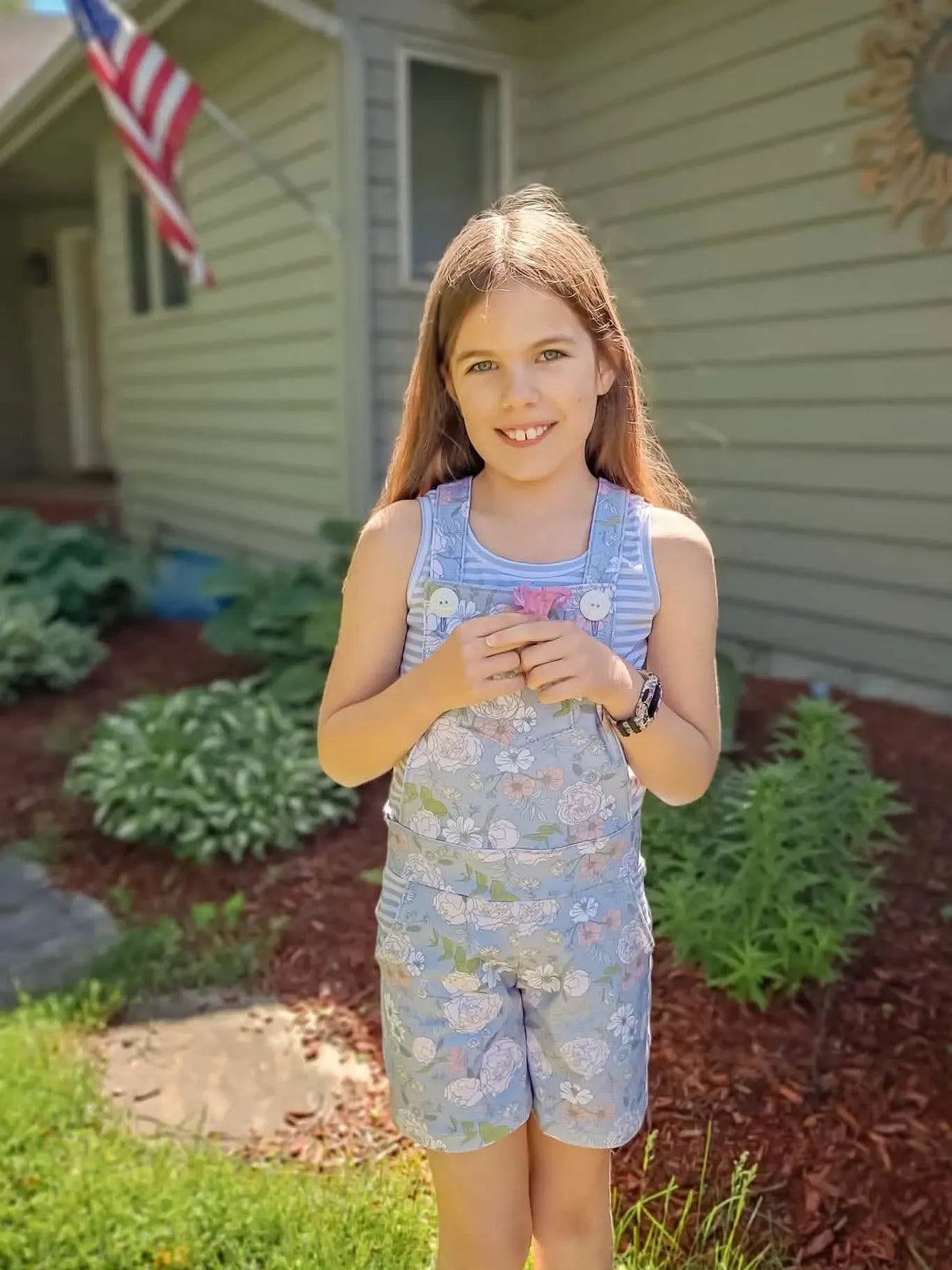 A girl wears dusty blue Japanese floral overalls over a striped tank top.