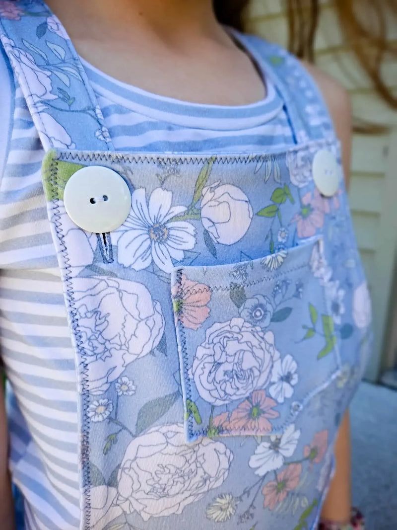 A person wears a dusty blue floral print overall with a striped shirt underneath.