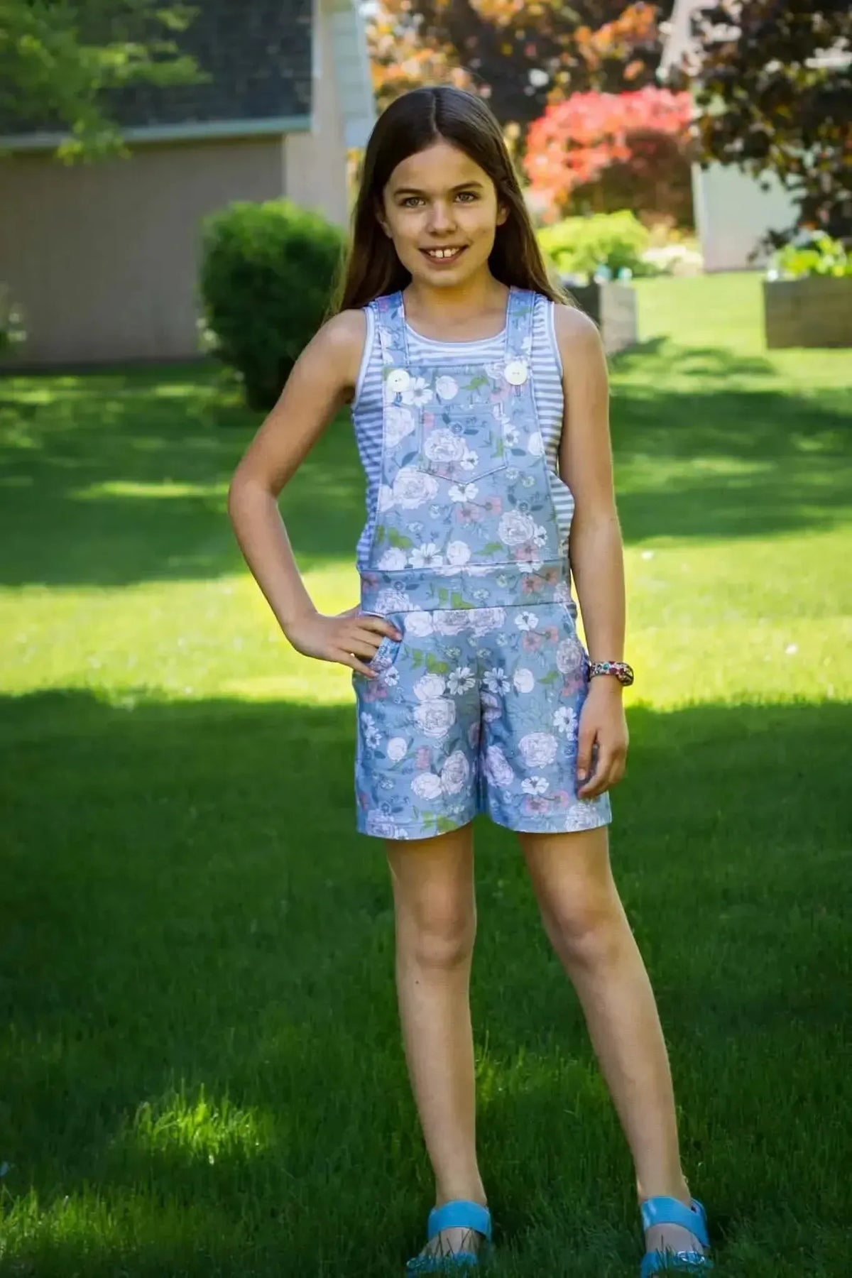Girl wearing a light blue floral short-sleeved romper in a garden.
