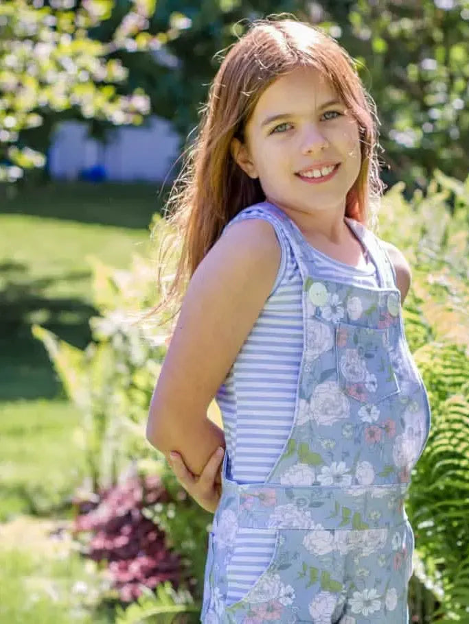 A young girl smiles, wearing a dusty blue Japanese floral print romper over a striped shirt.