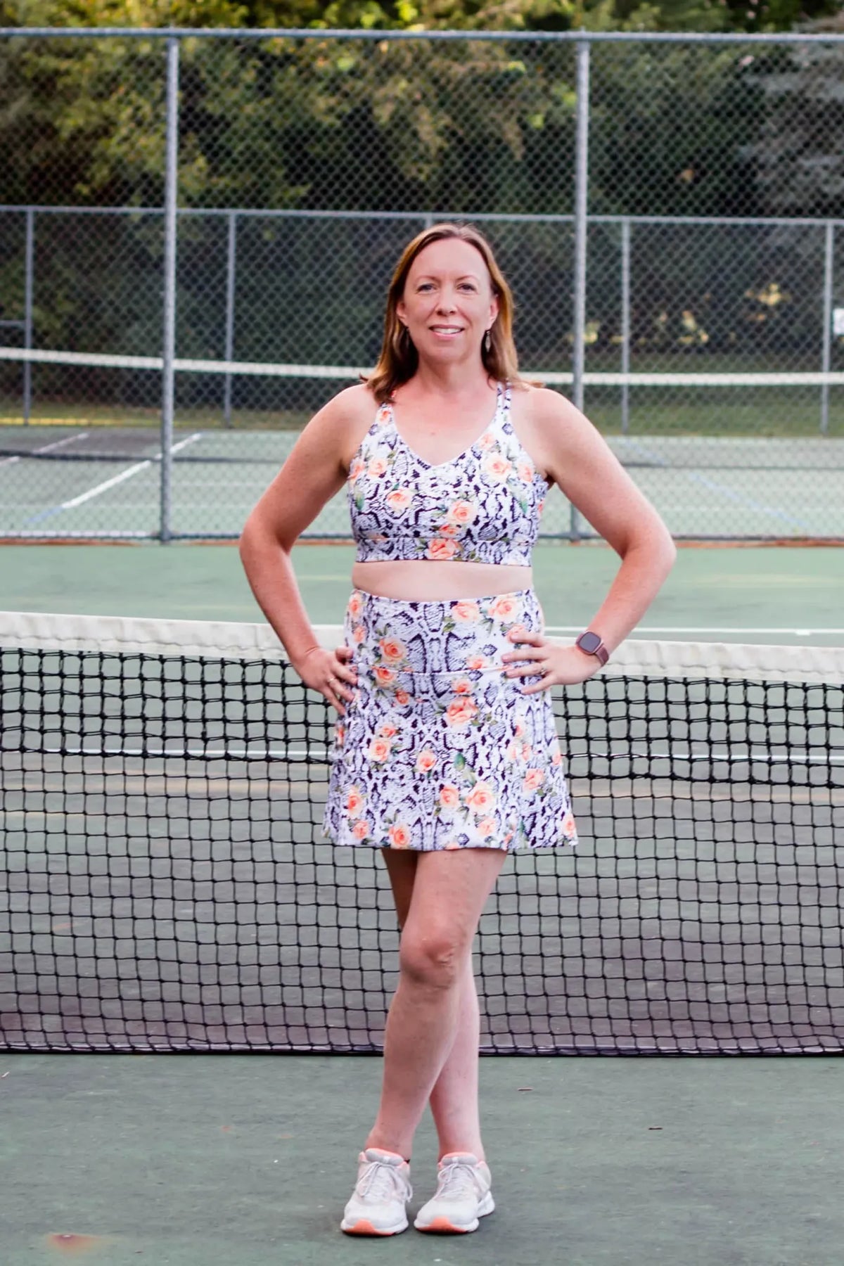 Woman in a floral snake print athletic top and skirt on a tennis court.