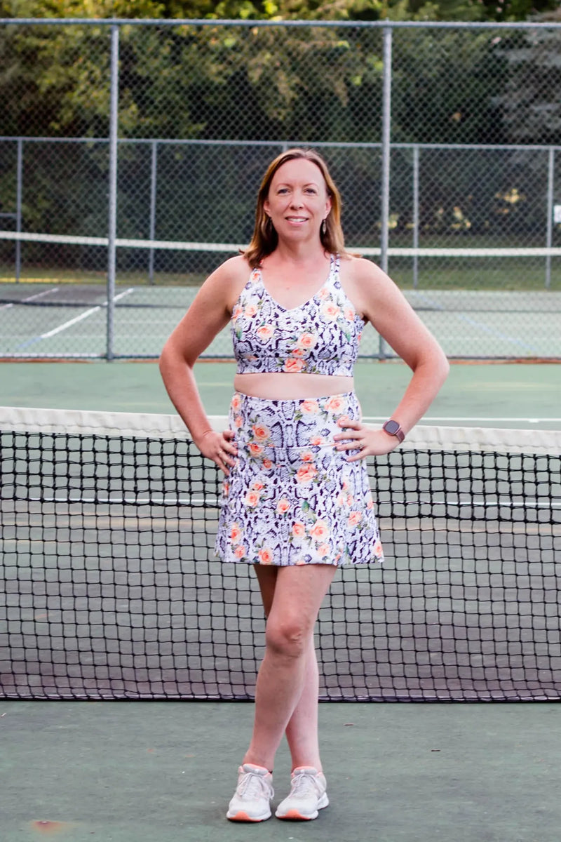 Woman in a floral snake print athletic top and skirt on a tennis court.