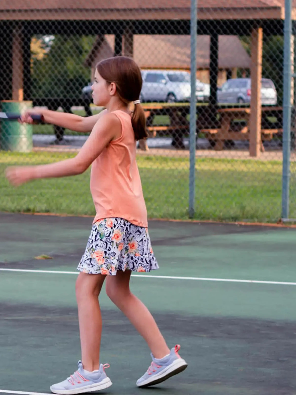A young girl in a floral snake print skirt plays tennis.