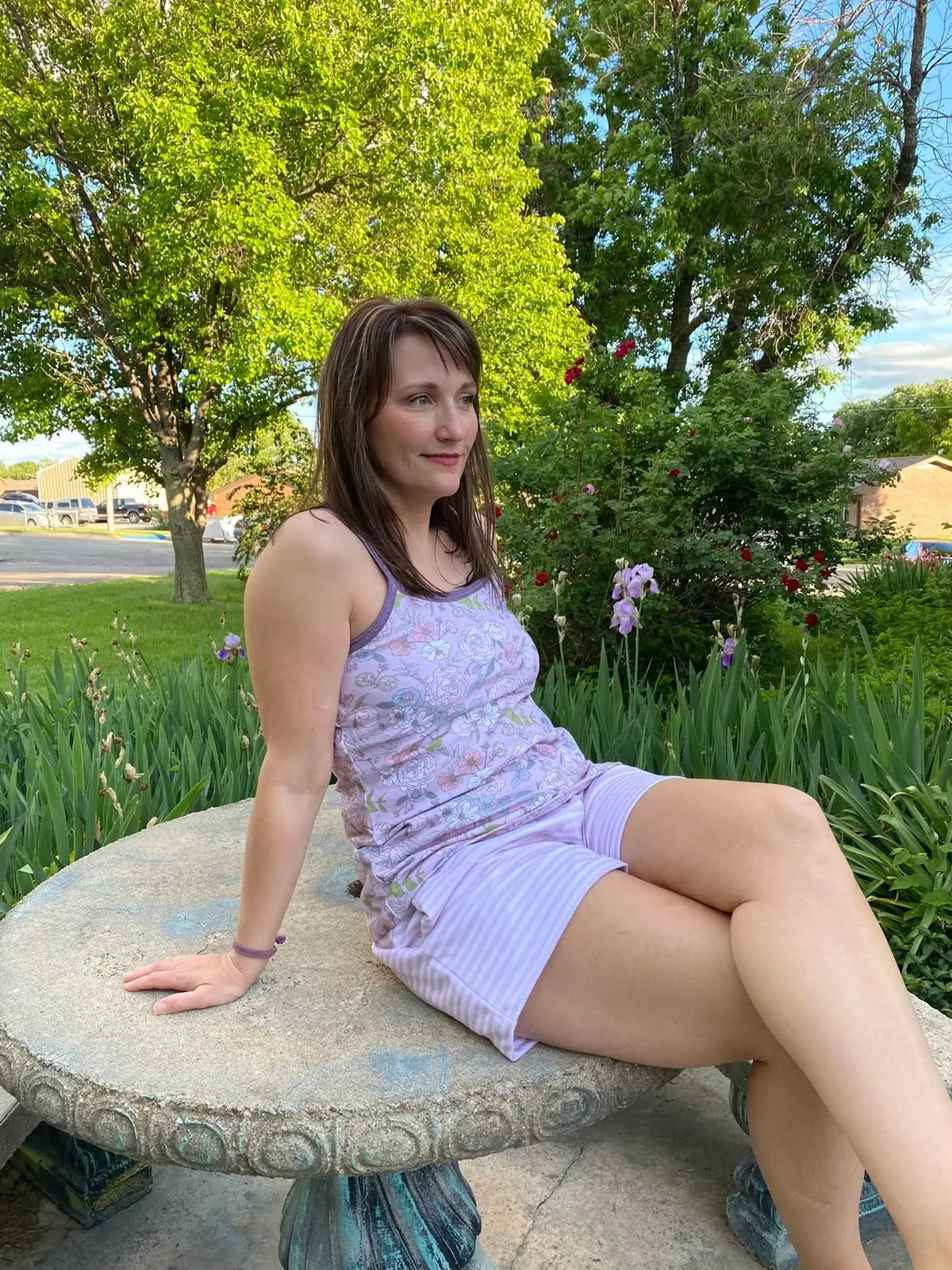 A woman in a mauve floral tank top and striped shorts sits on a stone table.