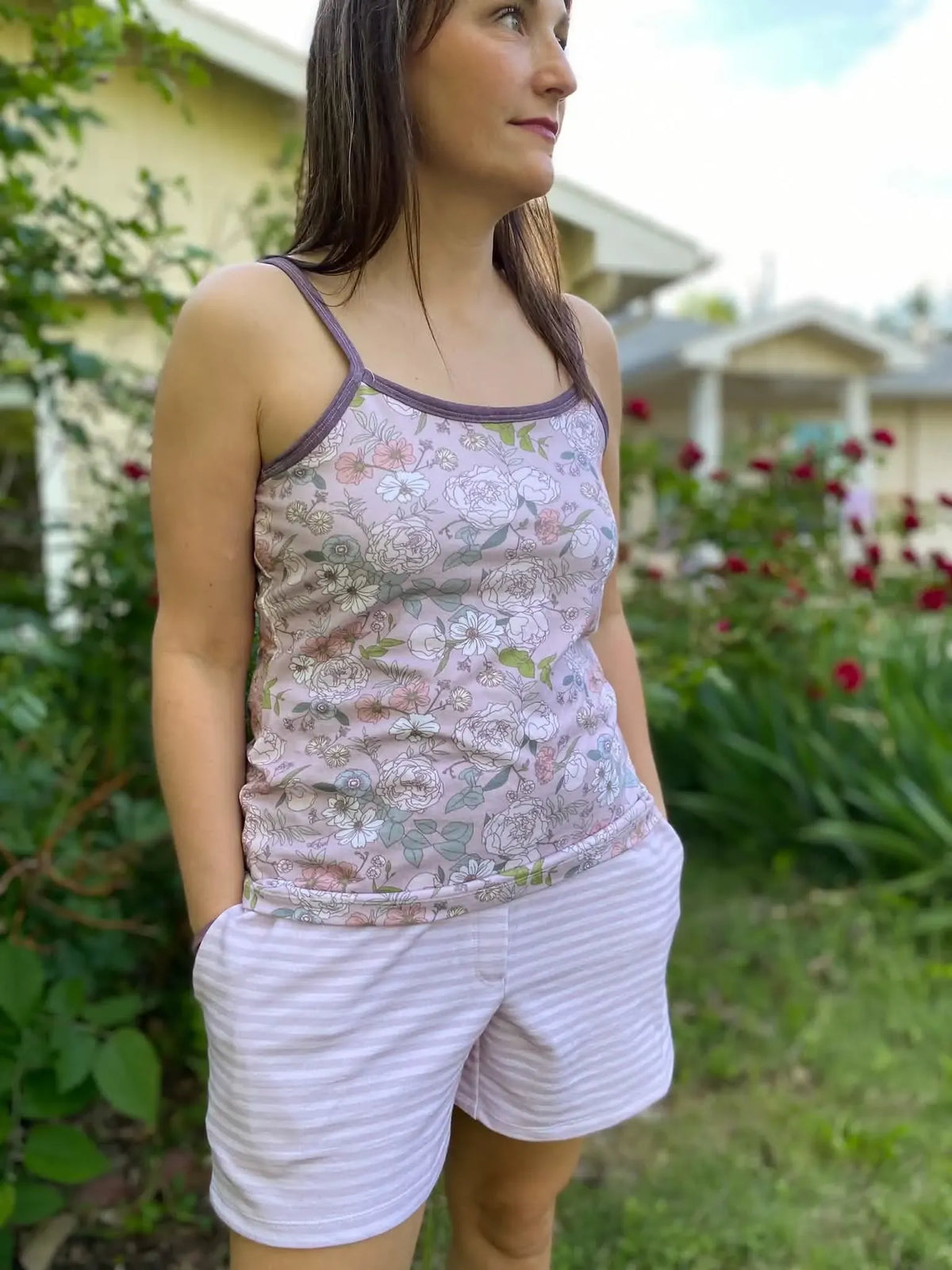 A woman wears a floral tank top and mauve striped shorts outdoors.