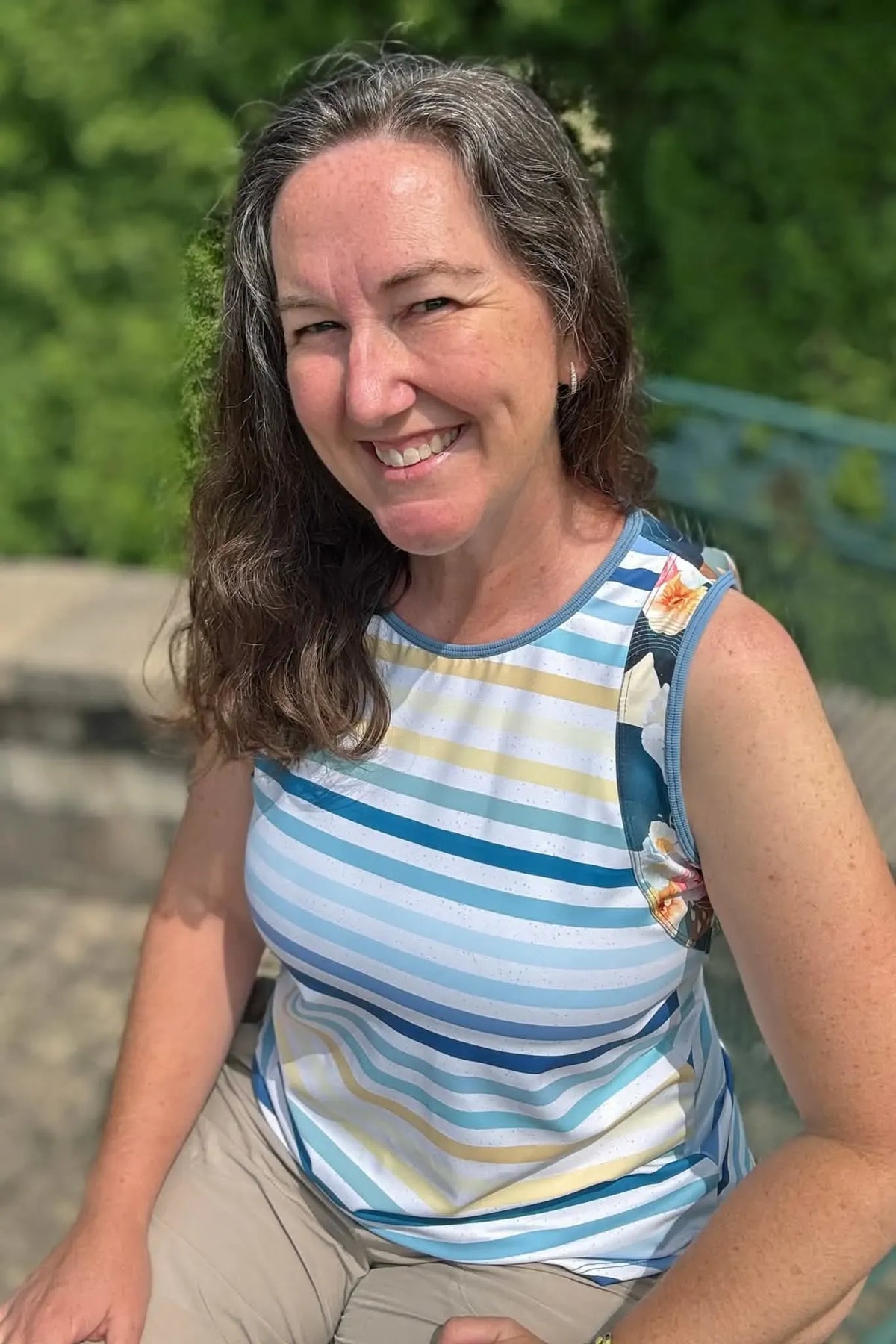 A woman smiles, wearing a striped tank top with floral accents.