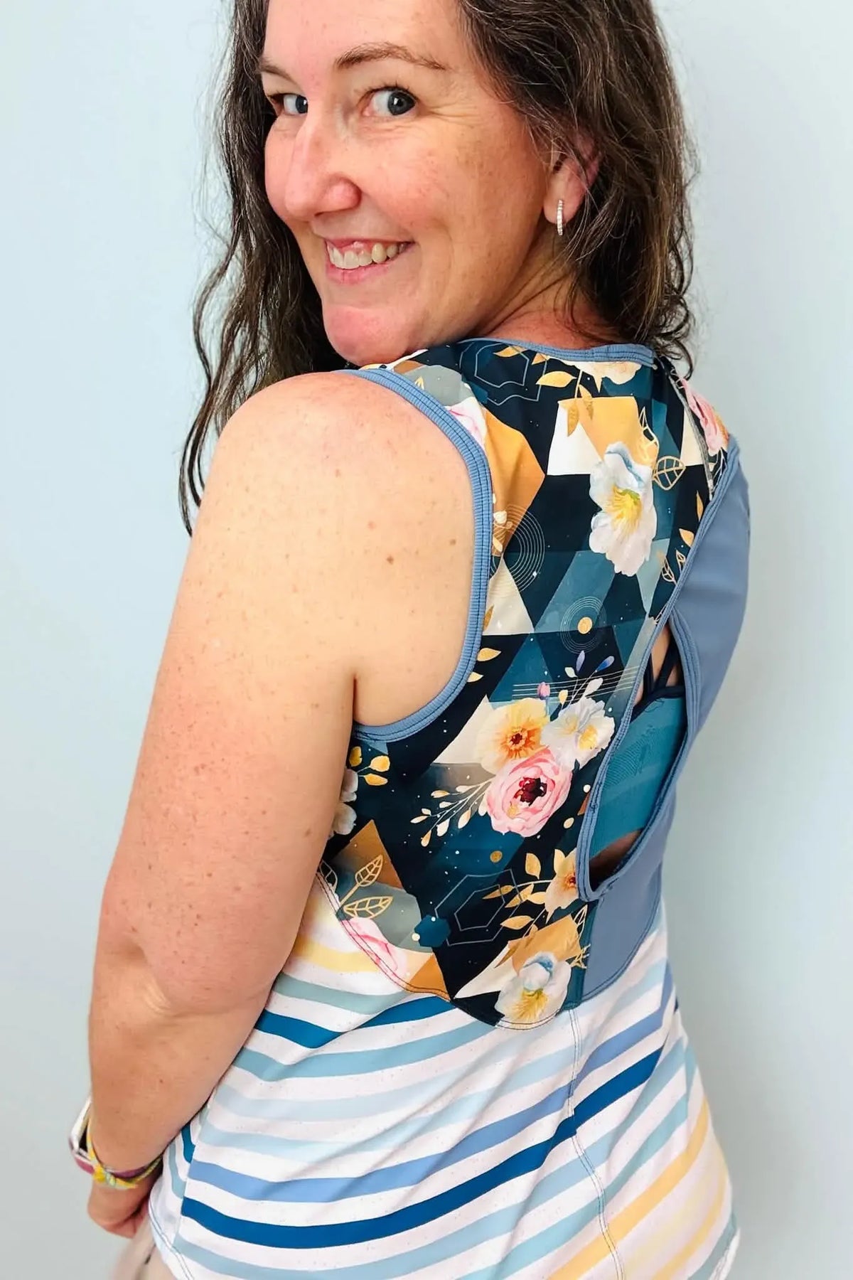 A woman smiles, wearing a top with a floral back and striped front.