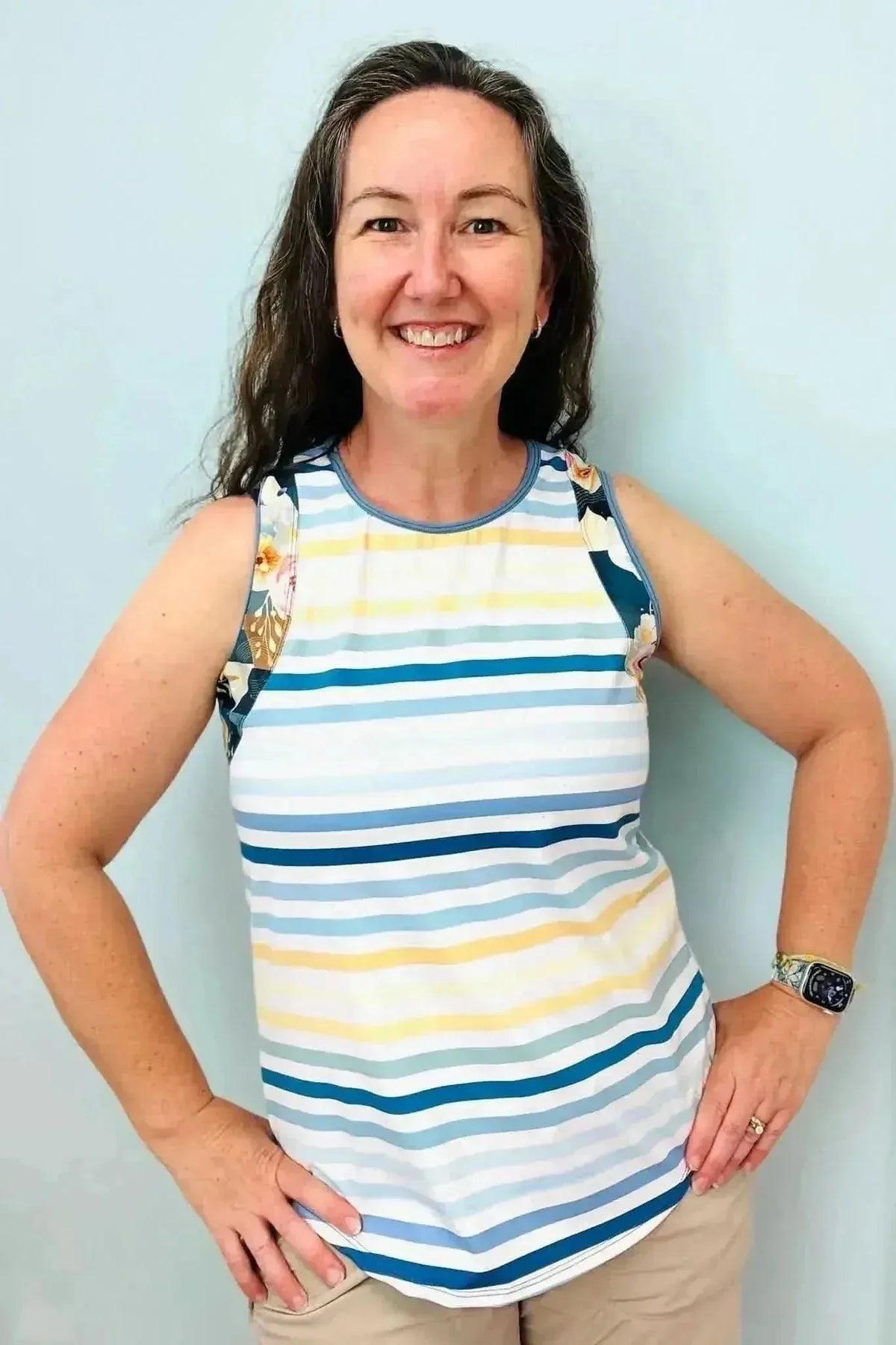 Woman modeling a sleeveless striped top in blue, white, and yellow with floral shoulder patches.