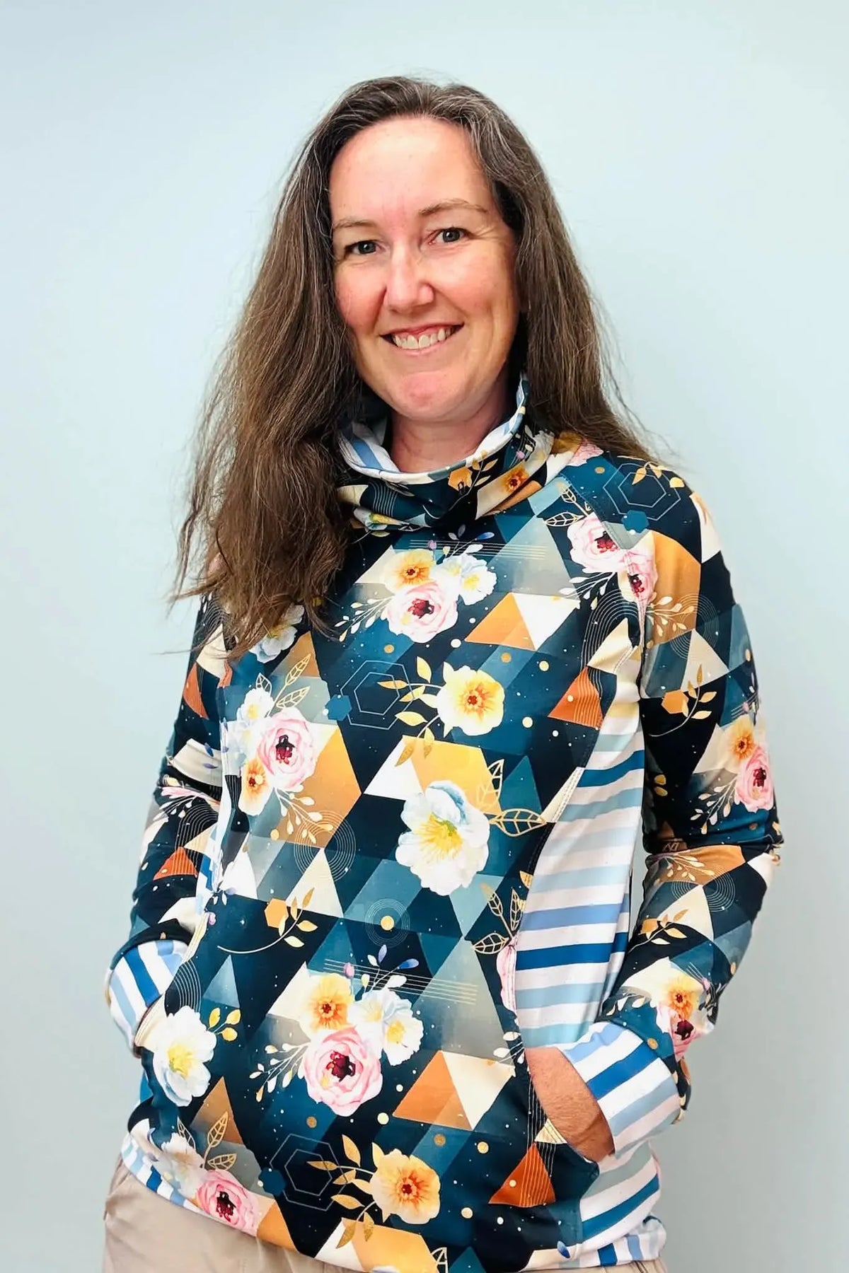 A woman smiles wearing a long-sleeved top with a floral and geometric pattern.