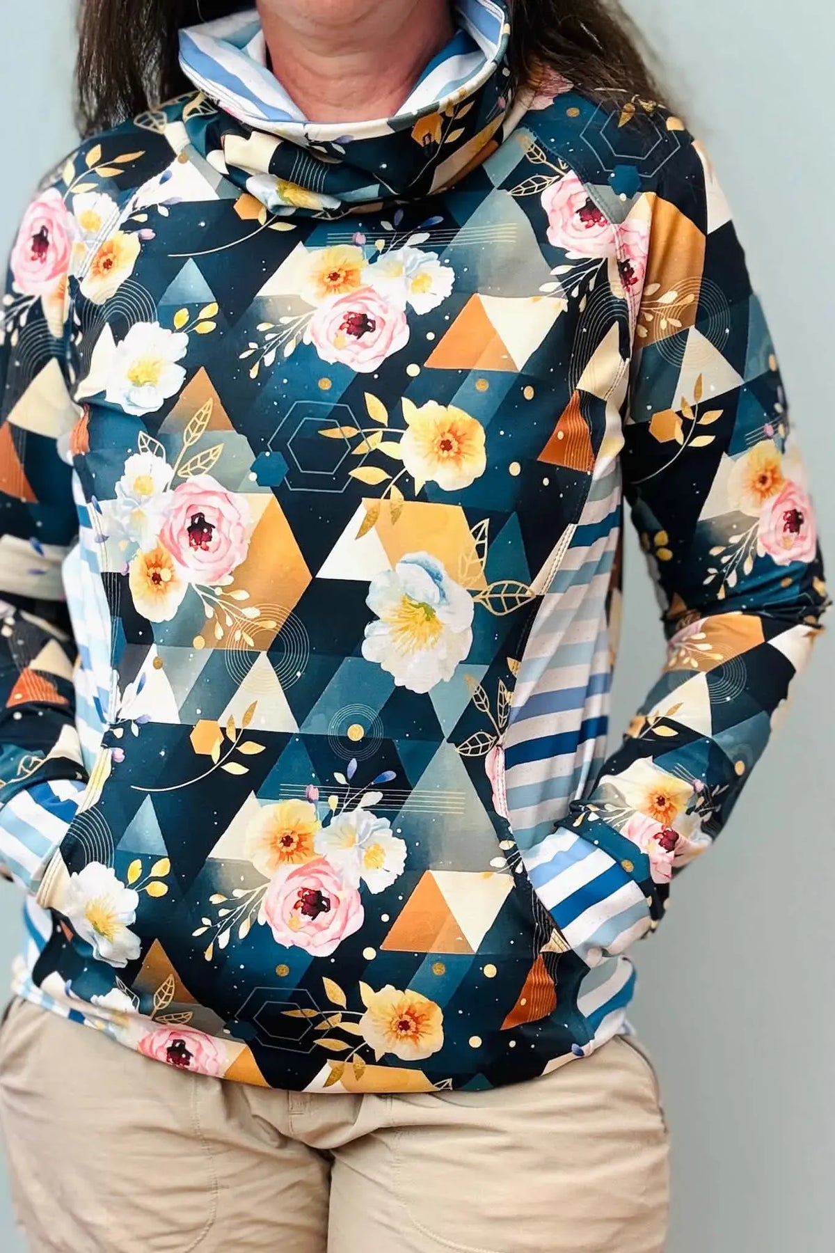 A person wears a floral and geometric patterned long-sleeved top with a cowl neck.