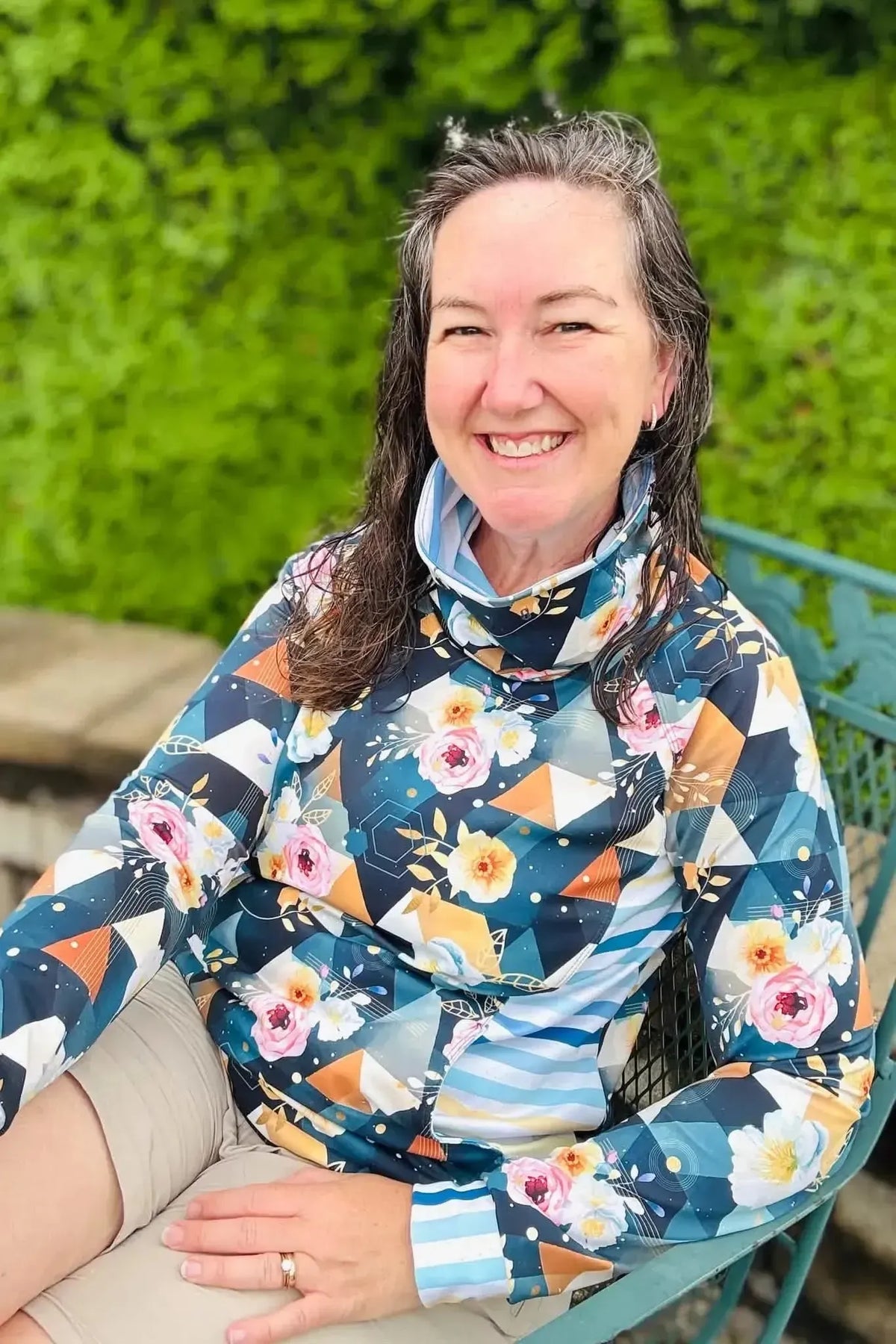 Woman wearing a dark teal geometric floral print top with collar, seated outdoors.