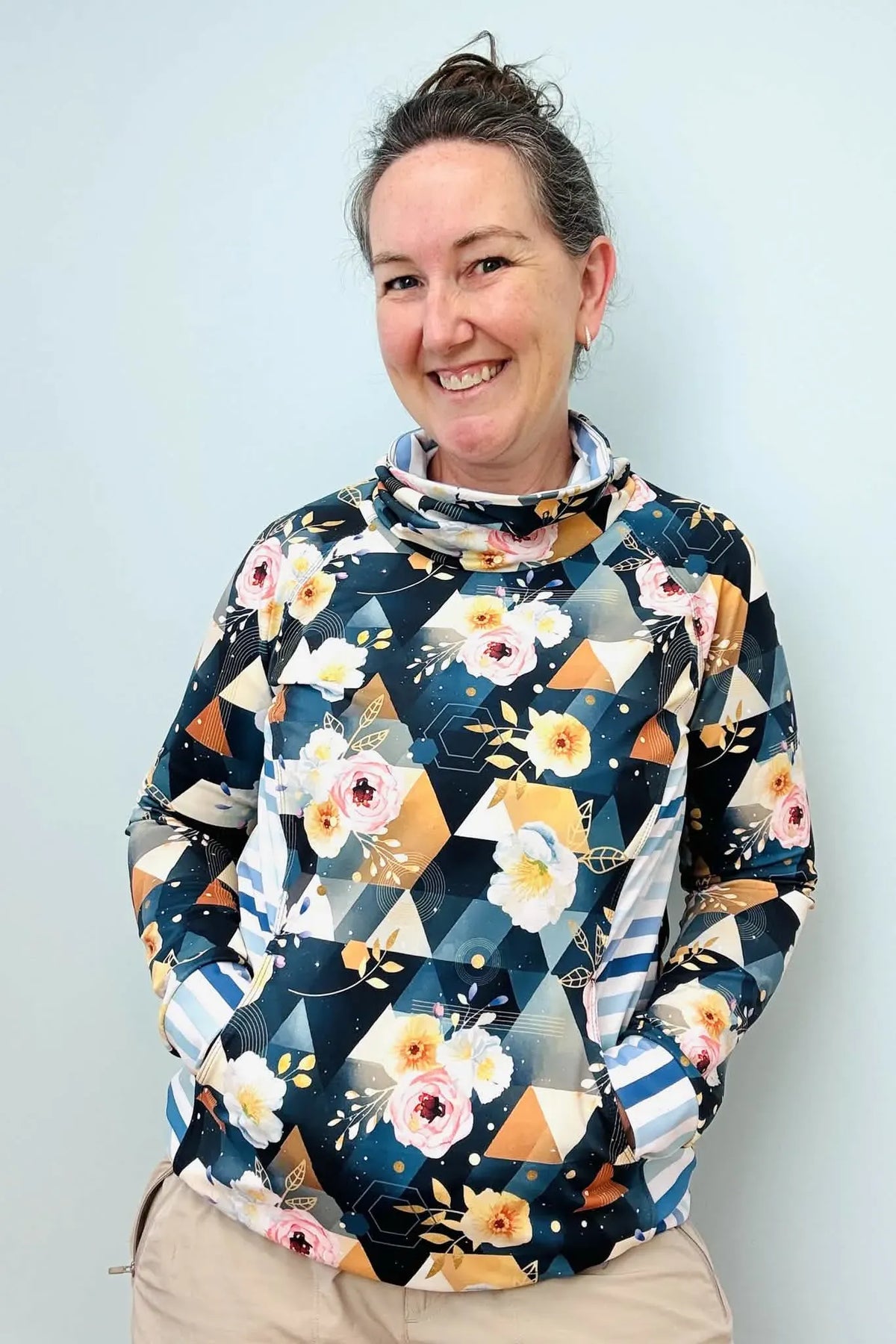 A woman smiles wearing a floral and geometric print cowl neck top with pockets.