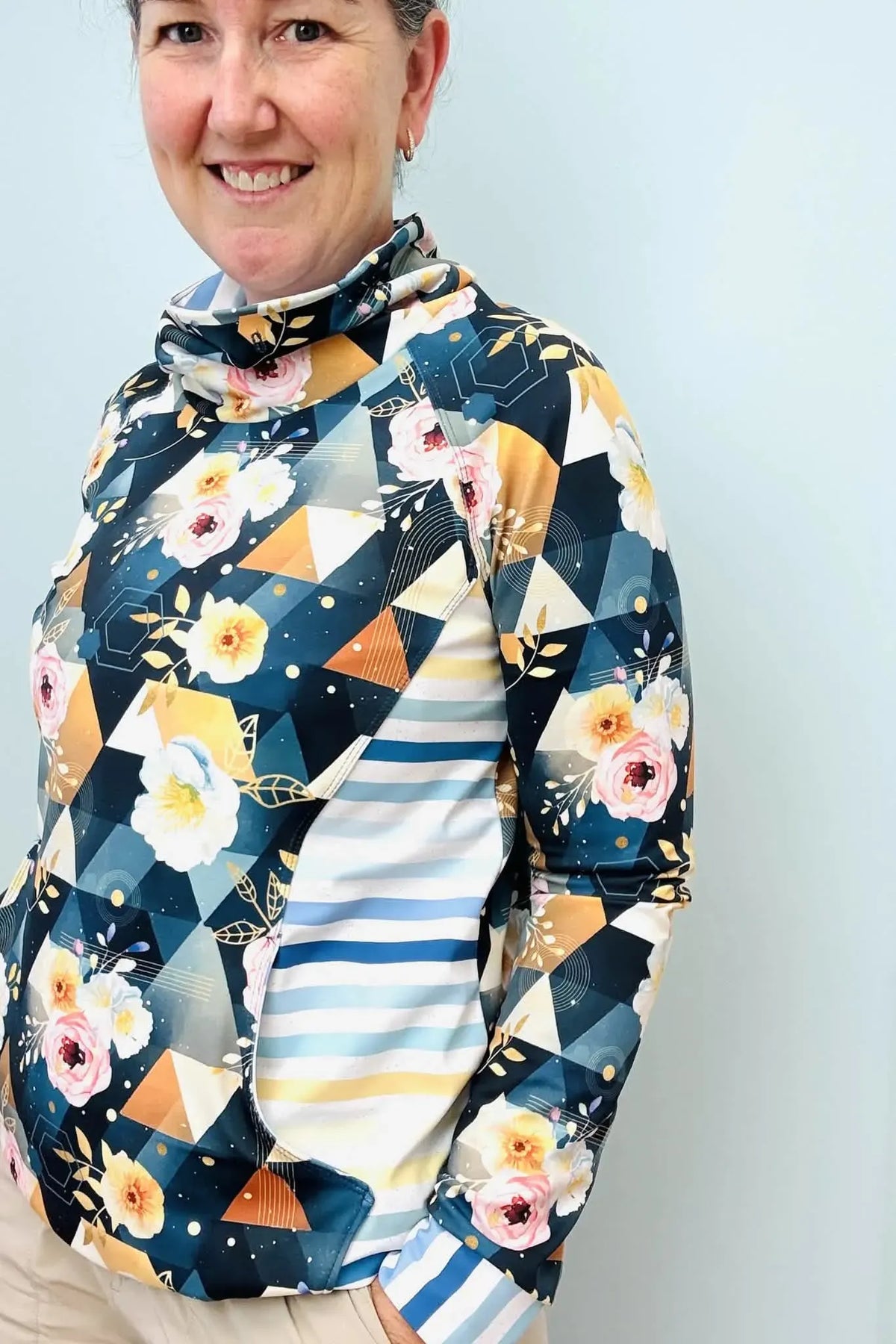 A woman smiles, wearing a floral and geometric print top with striped accents.