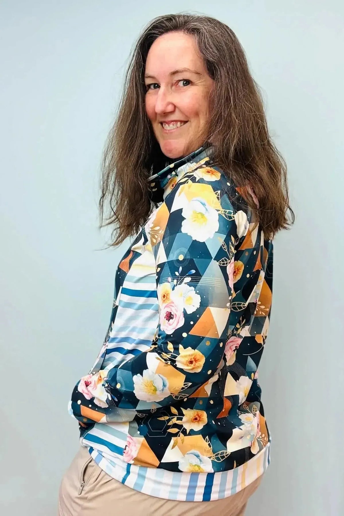 A woman models a dark teal geometric floral print jacket from behind on a light blue background.