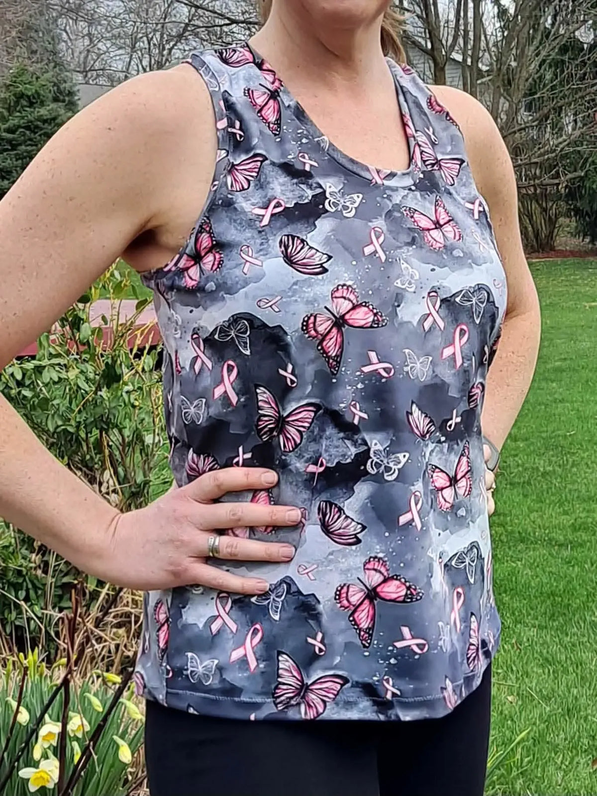 A woman wears a gray tank top with pink butterflies and breast cancer ribbons.