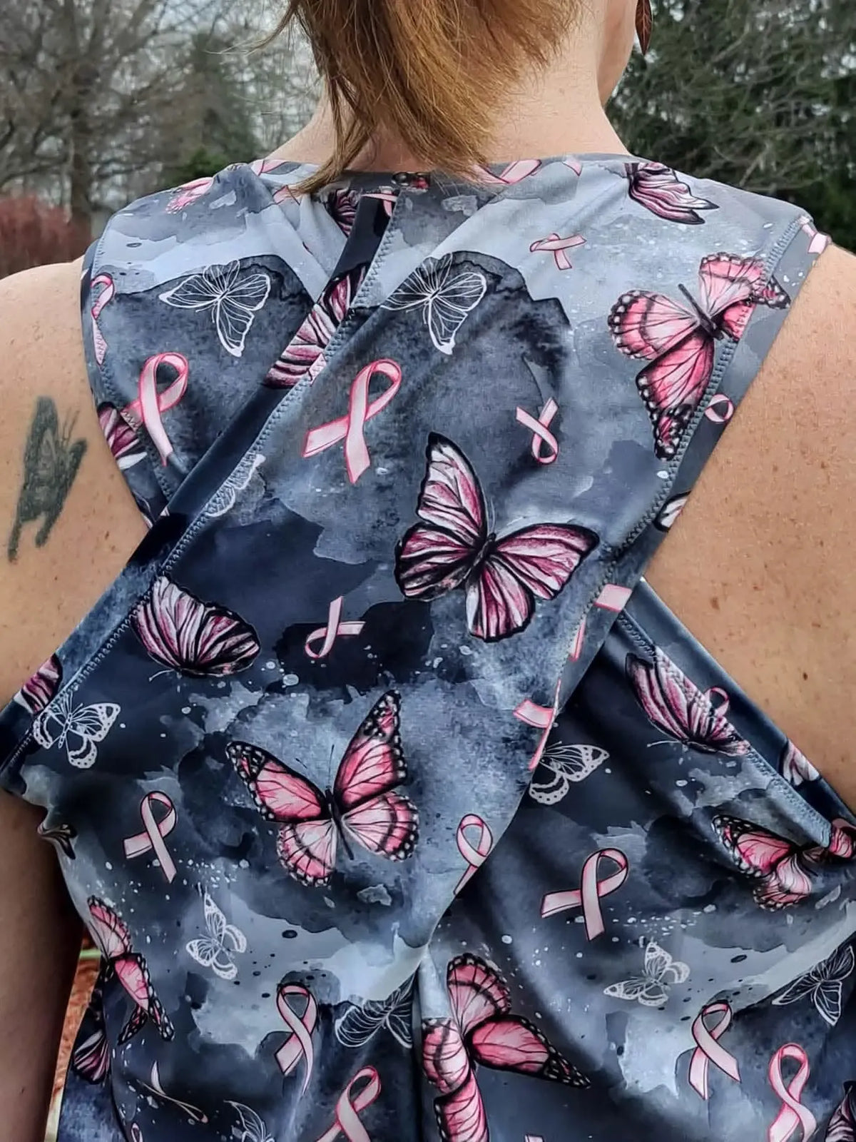 A person from behind wearing a top with pink ribbons and butterflies.