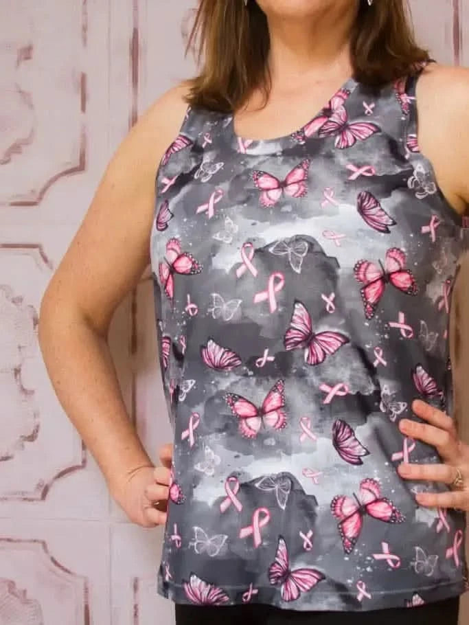 A woman models a sleeveless top with a gray background, pink butterflies, and pink ribbons.